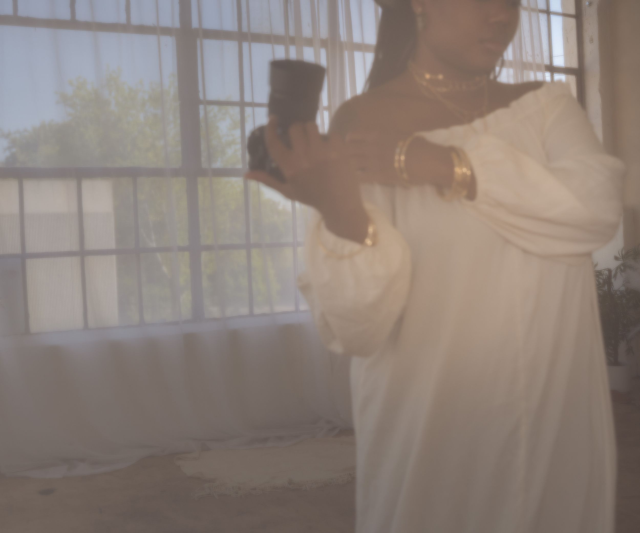 A figure in flowy white fabric stands in a sunlit room with window light creating an ethereal atmospheric effect.
