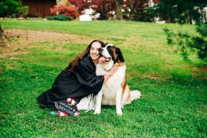 A Saint Bernard dog sits on green grass next to someone wearing a black dress on a sunny day.