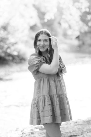 Black and white portrait of a person in a ruffled summer dress posing outdoors in a dreamy natural setting.