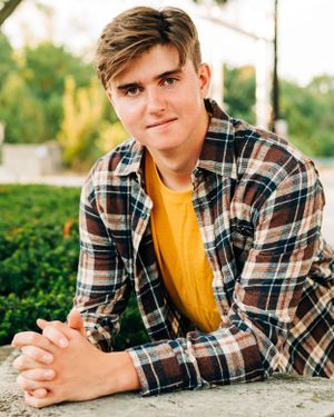 Someone wearing a yellow t-shirt and plaid flannel shirt poses outdoors in natural lighting.
