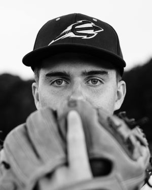 Black and white portrait of baseball player peeking through baseball glove in closeup shot.