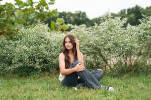 Someone sits on grass wearing casual attire near white flowering bushes on a summer day.