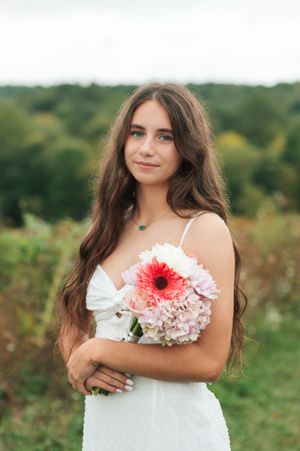 A bride in a white dress holds a beautiful bouquet of pink dahlias and gerbera daisies in a meadow.