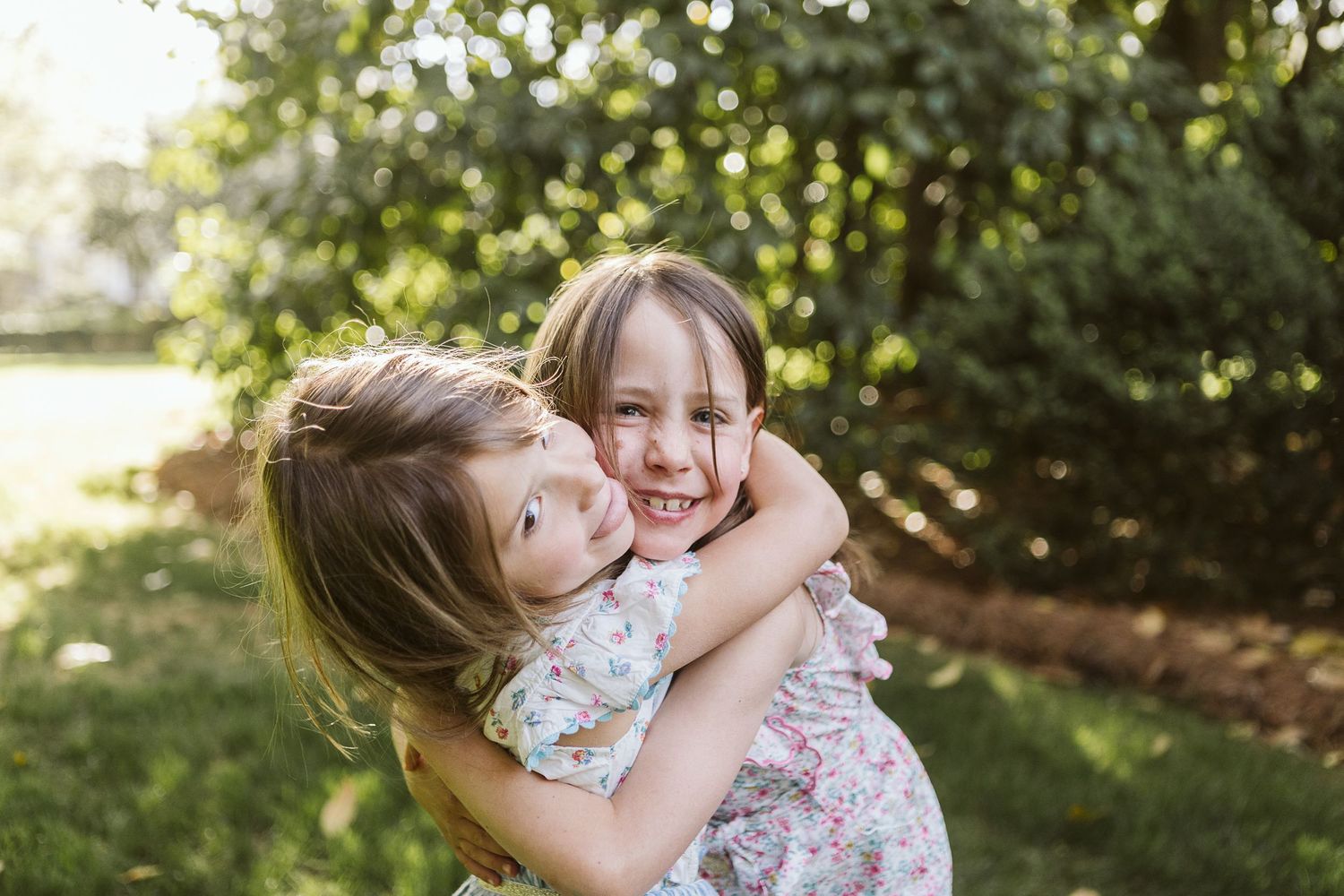 Sweet outdoor portrait of two young girls hugging in matching spring dresses during a family shoot