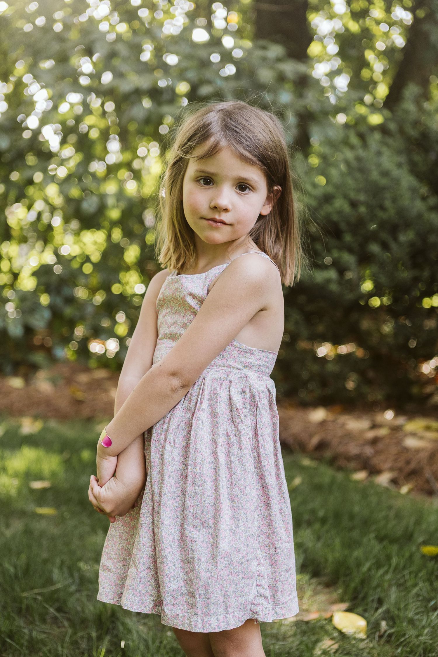 Sweet outdoor portrait of child standing and smiling in natural sunlight and lush greenery, dressed for spring