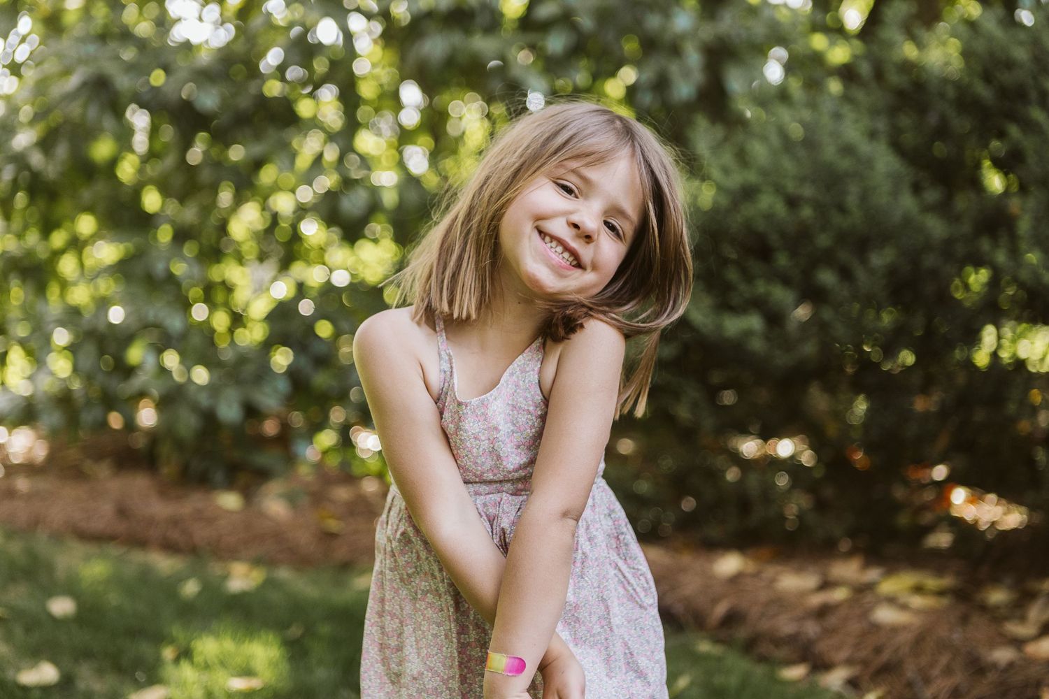 Sweet outdoor portrait of child smiling in natural sunlight and greenery, dressed for spring