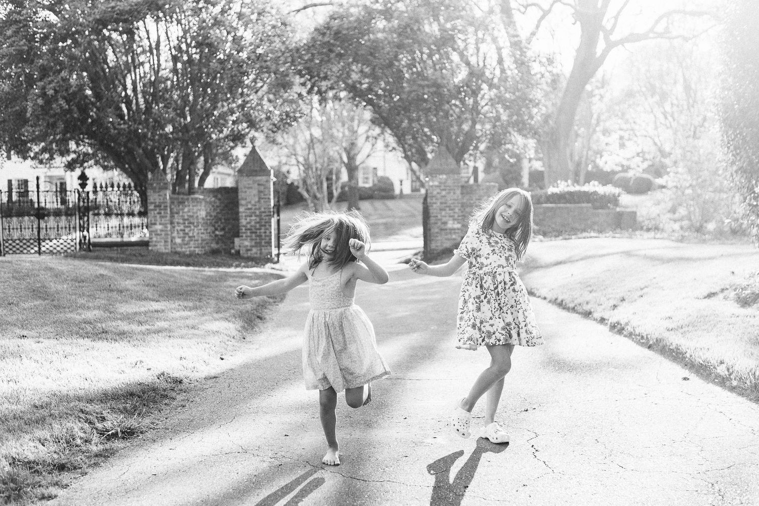 Two young girls dancing joyfully during a sunlit family photo session, in black and white
