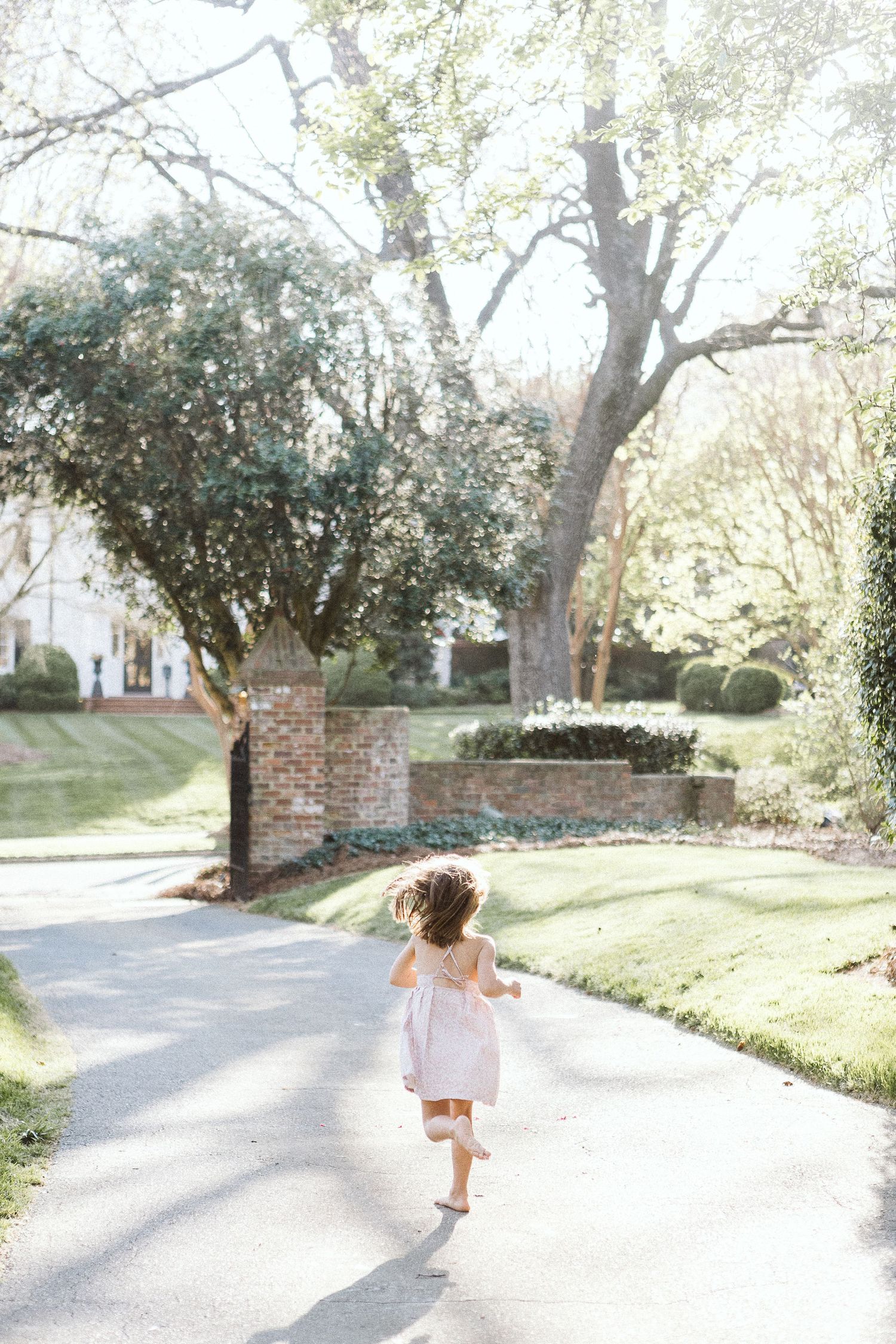 Young girl in motion, running joyfully outside in a sunlit pathway during a natural light photo session