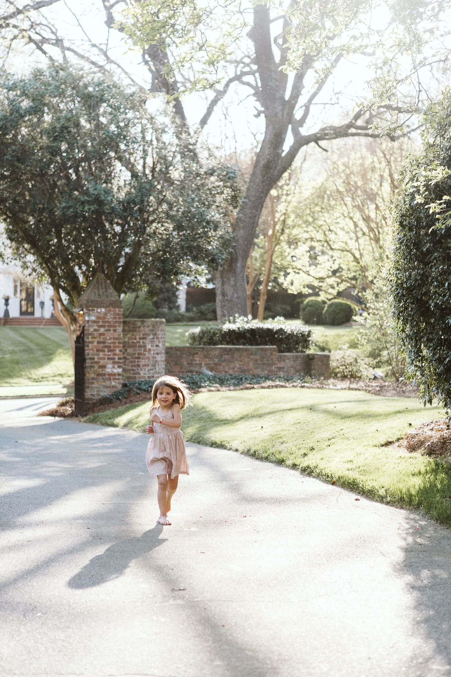 Young girl in motion, playing joyfully outside in a sunlit path during a natural light photo session