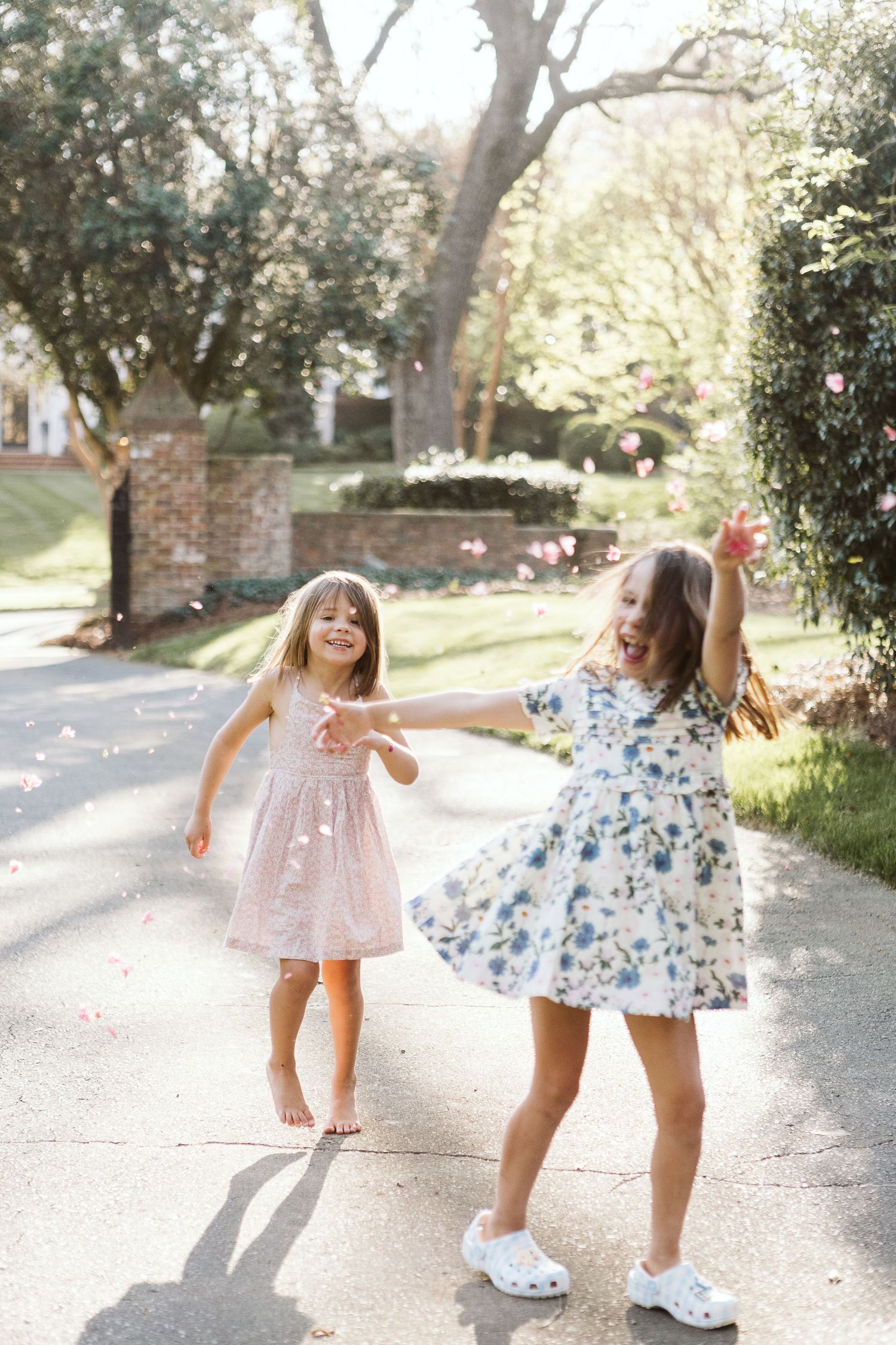 Two young girls dancing joyfully during a sunlit family photo session