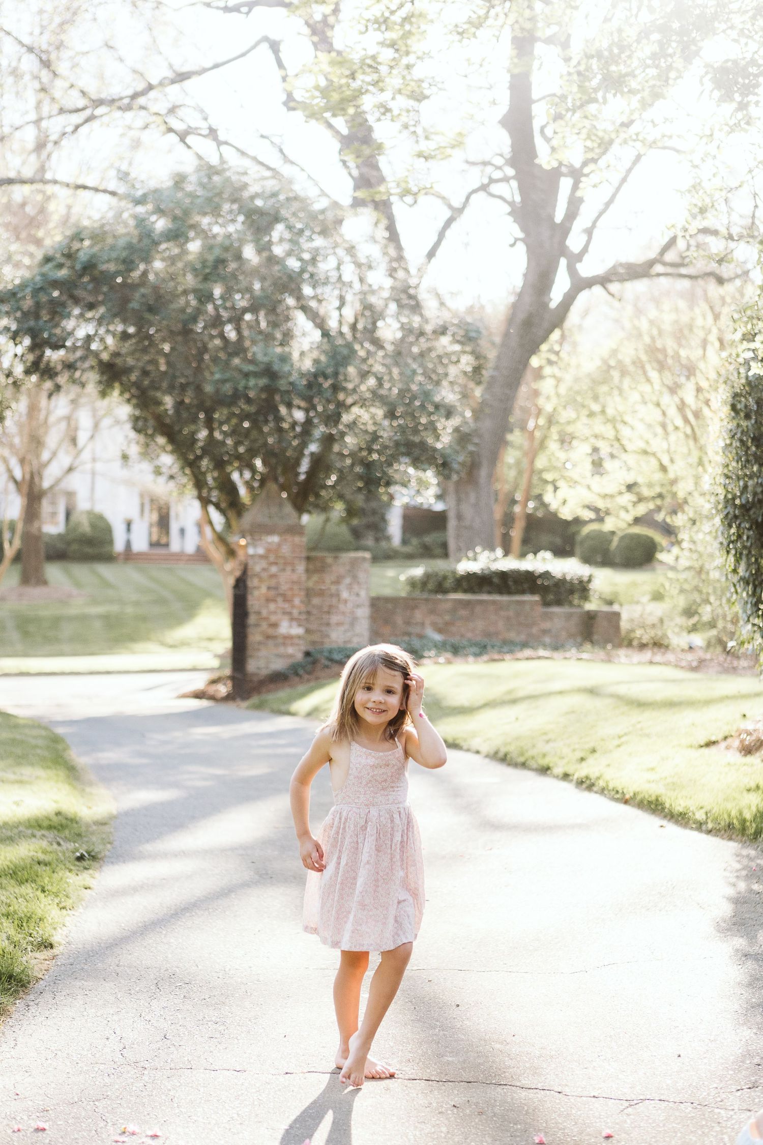 A sweet portrait of a young girl smiling outside during a sunlit family photo session, dressed for spring