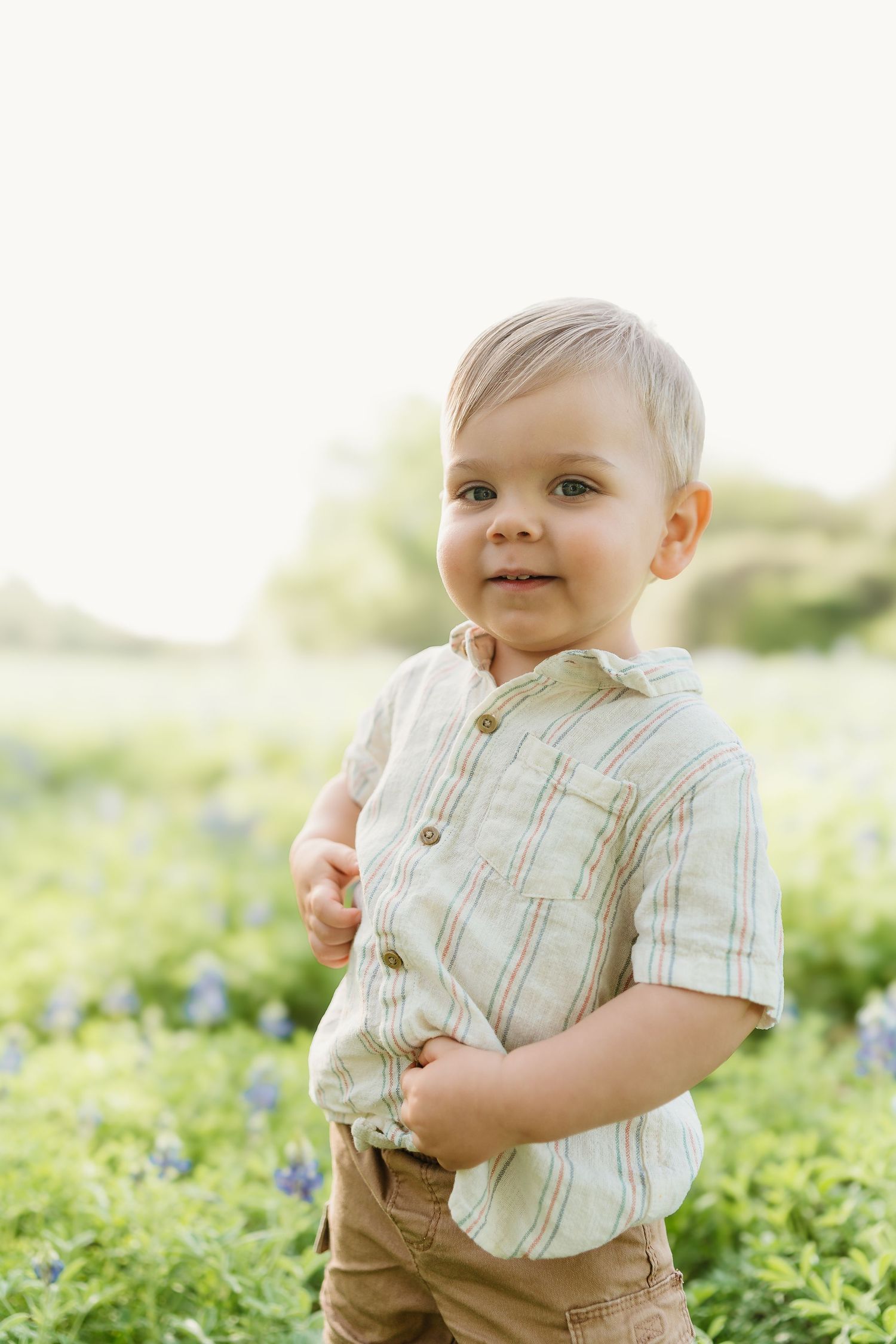 A toddler in a striped shirt plays in a field of bluebonnets during springtime.
