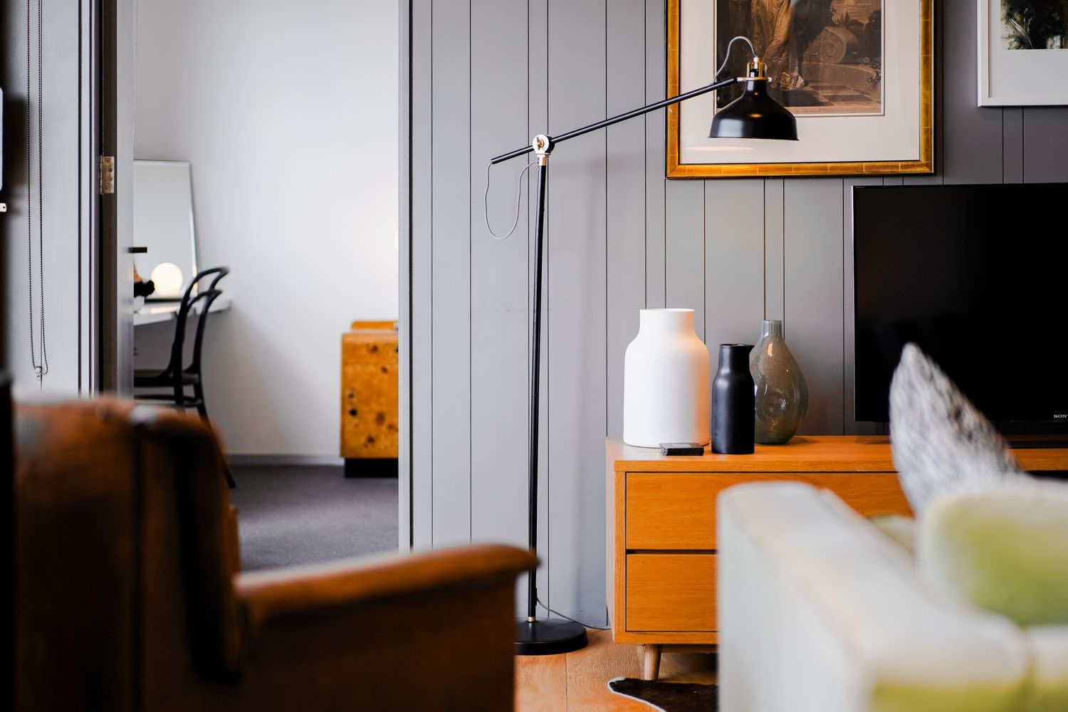 Modern interior with gray walls, wooden furniture, and a sleek floor lamp next to storage cabinet.
