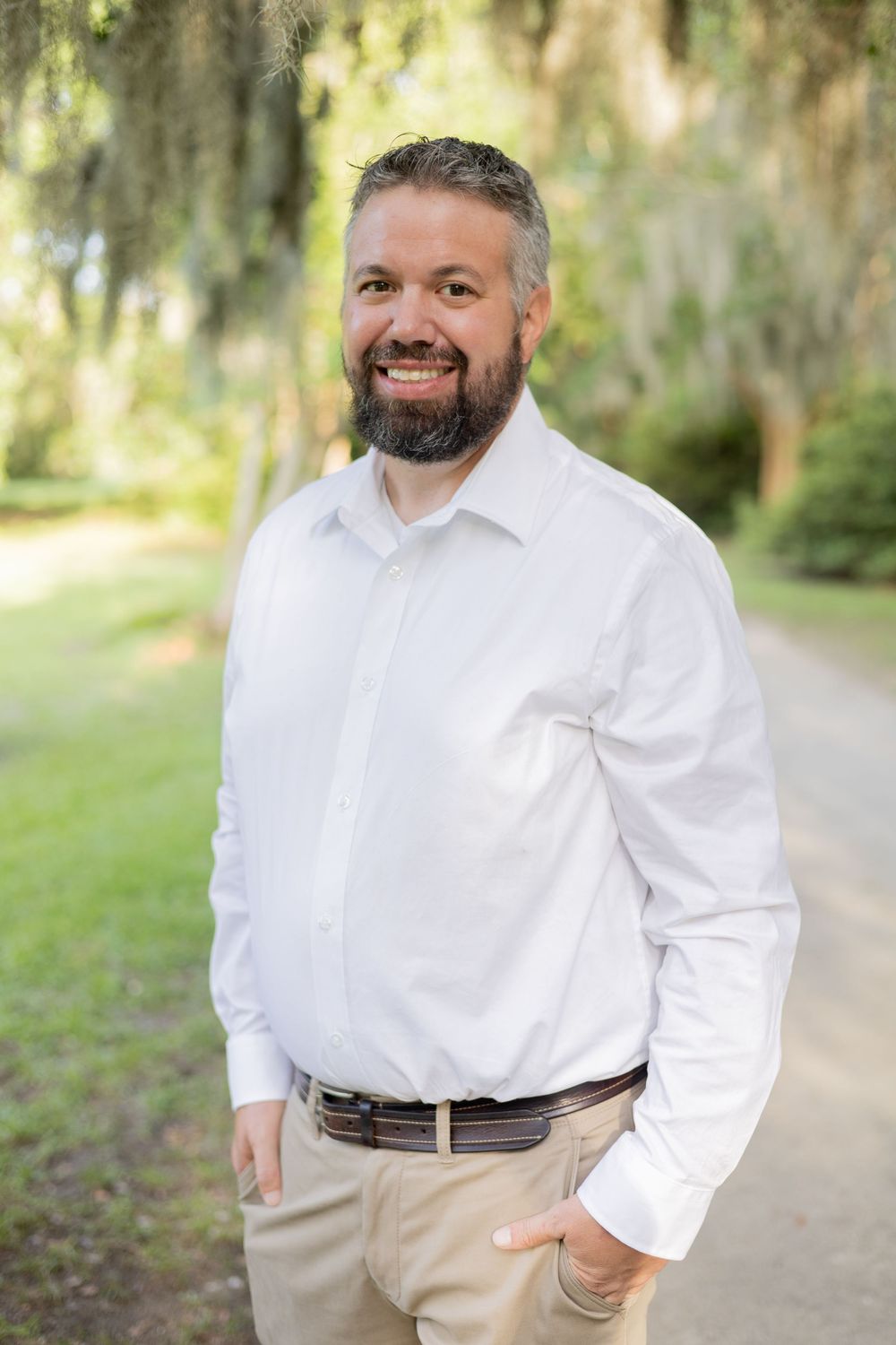 Professional outdoor portrait in a white dress shirt and khakis standing on a path with Spanish moss and foliage in background.