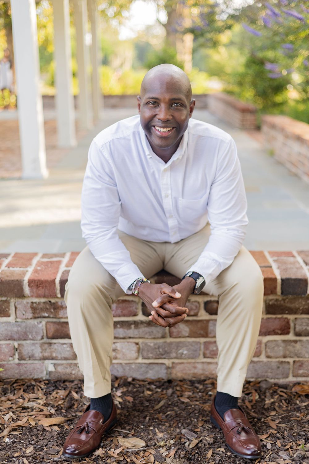 Professional portrait of someone in a crisp white button-down shirt and khaki pants sitting on a brick wall outdoors.
