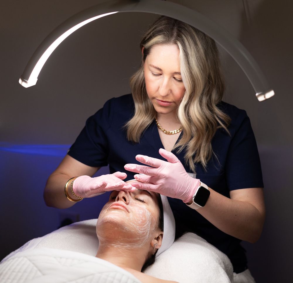 Medical professional performs a facial treatment on client lying on treatment table with curved light trails in background.