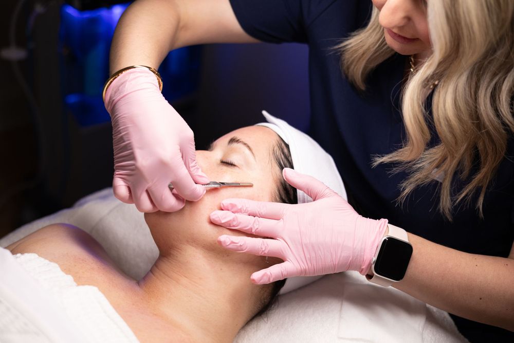 Esthetician wearing pink gloves performs a facial treatment while wearing a smart watch at a spa.