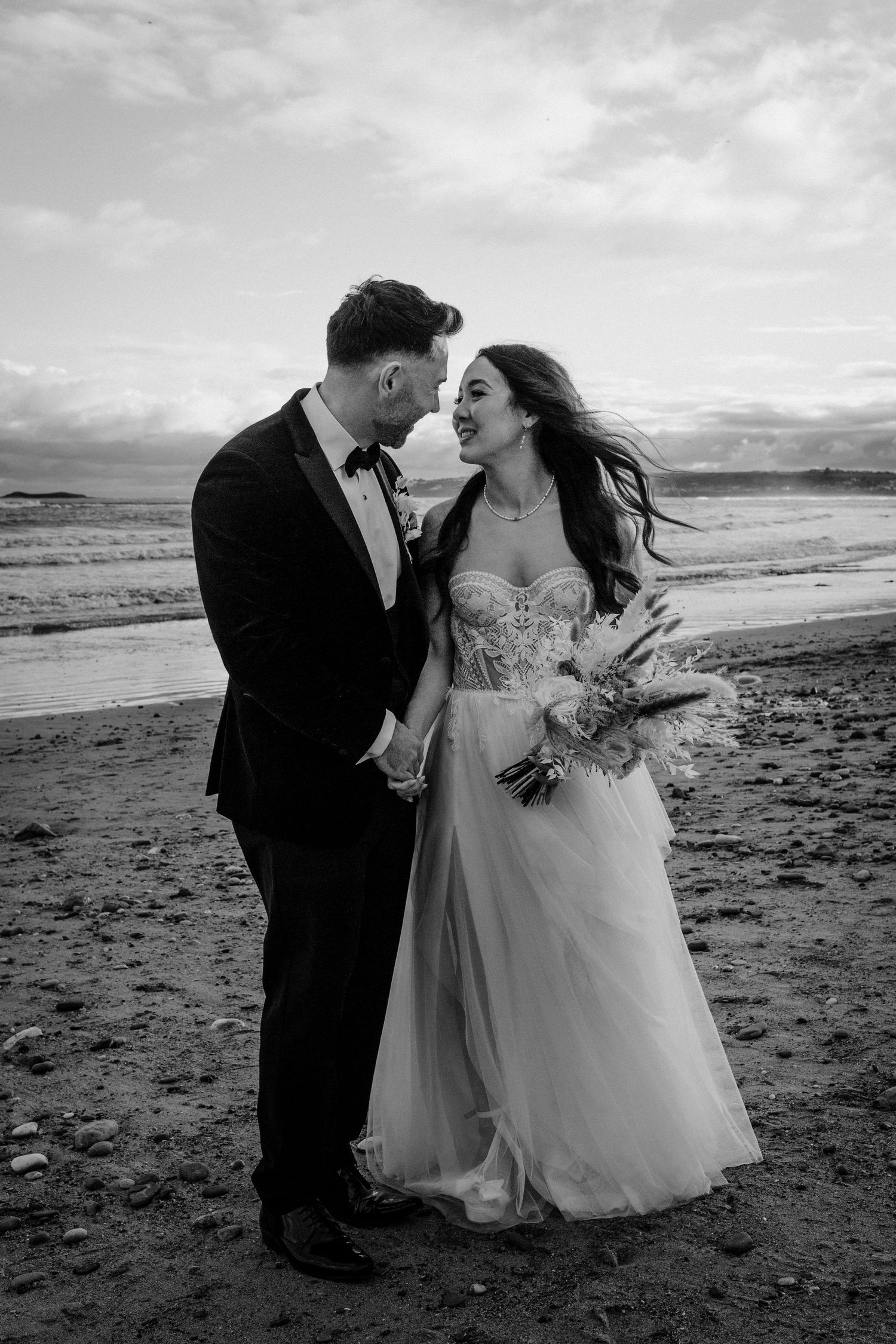 A romantic black and white wedding photo of a couple sharing an intimate moment on a beach at sunset.