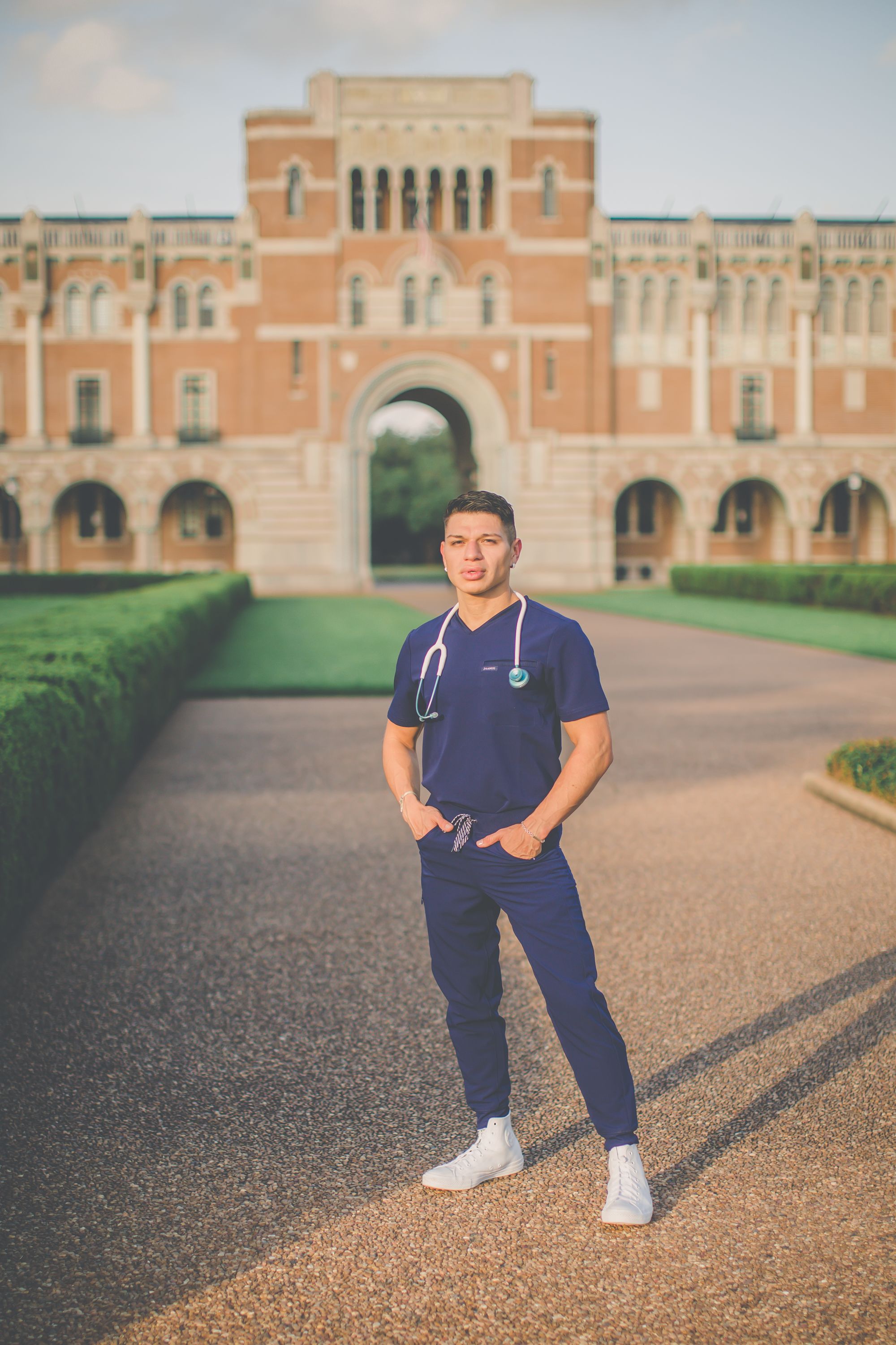 Medical professional poses in navy scrubs in front of grand university architecture.