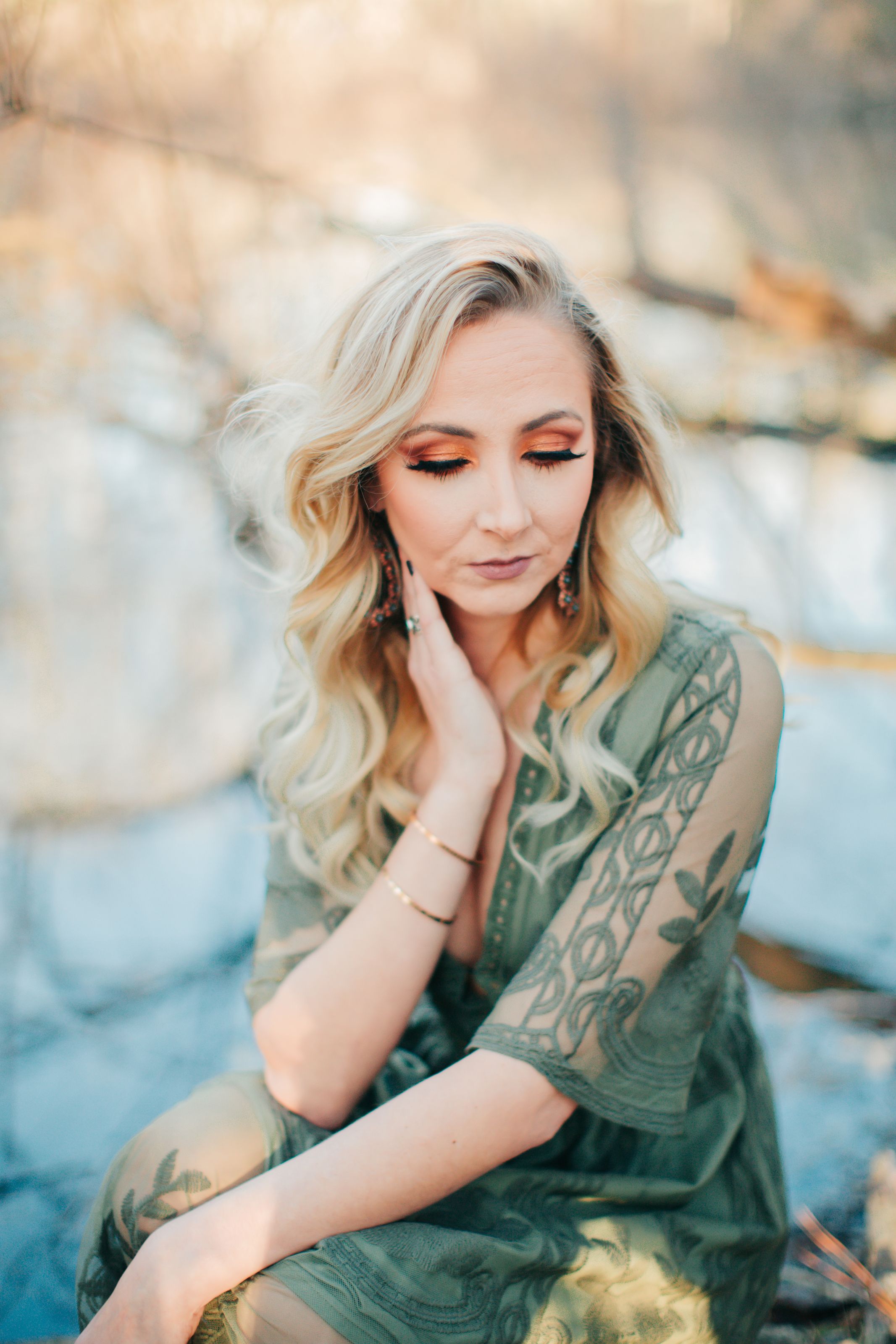 Artistic portrait of a person with blonde hair and tattoos in green dress posing outdoors at sunset.