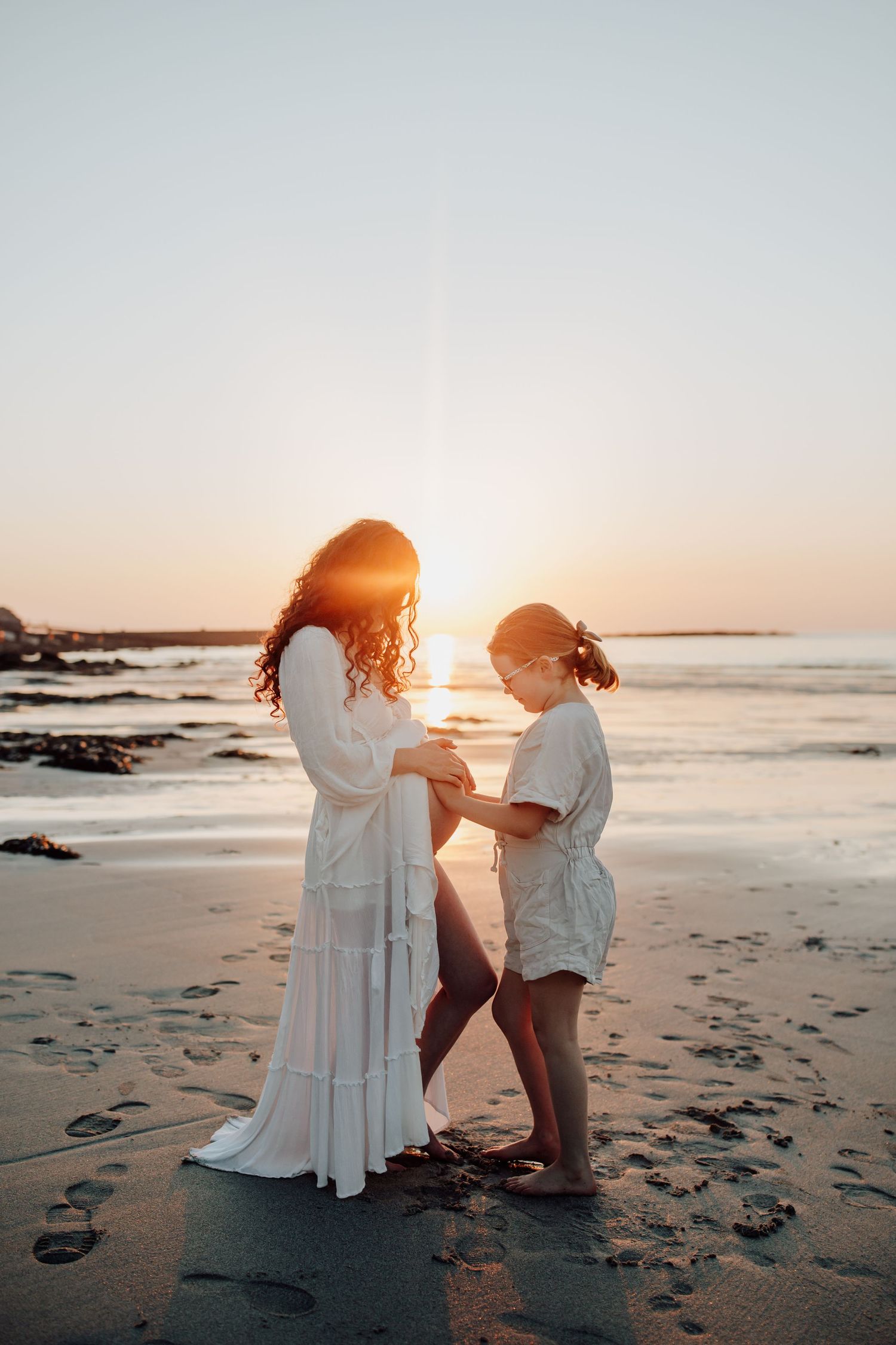 Silhouettes of people in white dresses standing on beach during golden sunset with ocean waves in background.