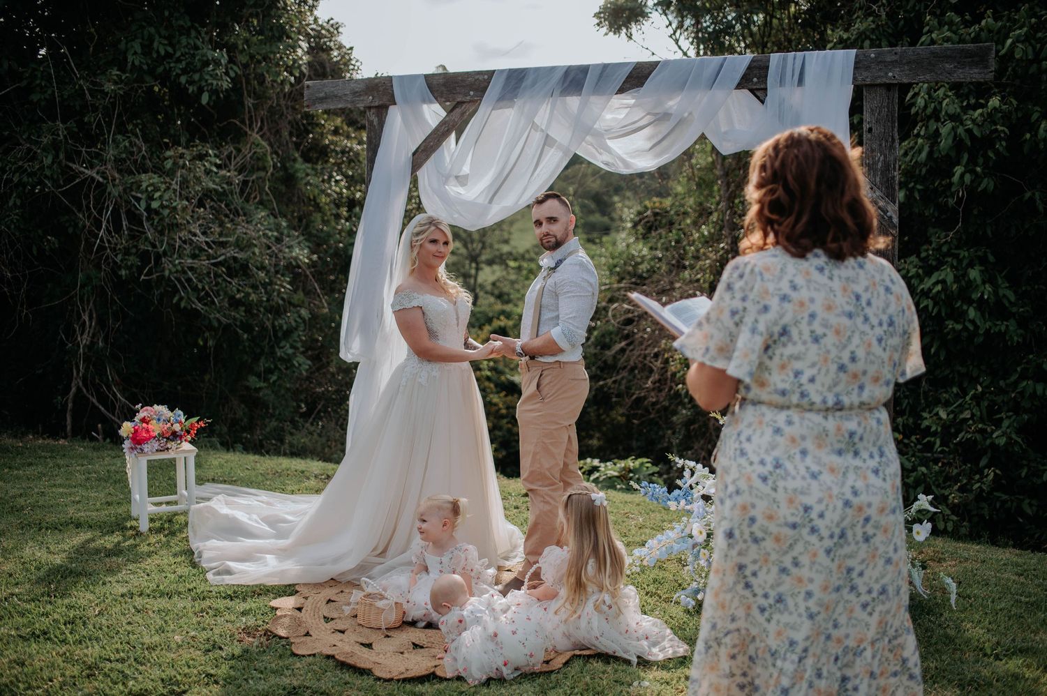 Outdoor wedding ceremony under white fabric arch with guests gathered on lawn.