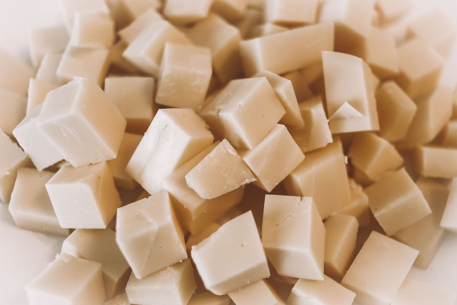 Close-up of uniform beige diced tofu cubes arranged in a pile on a white surface.