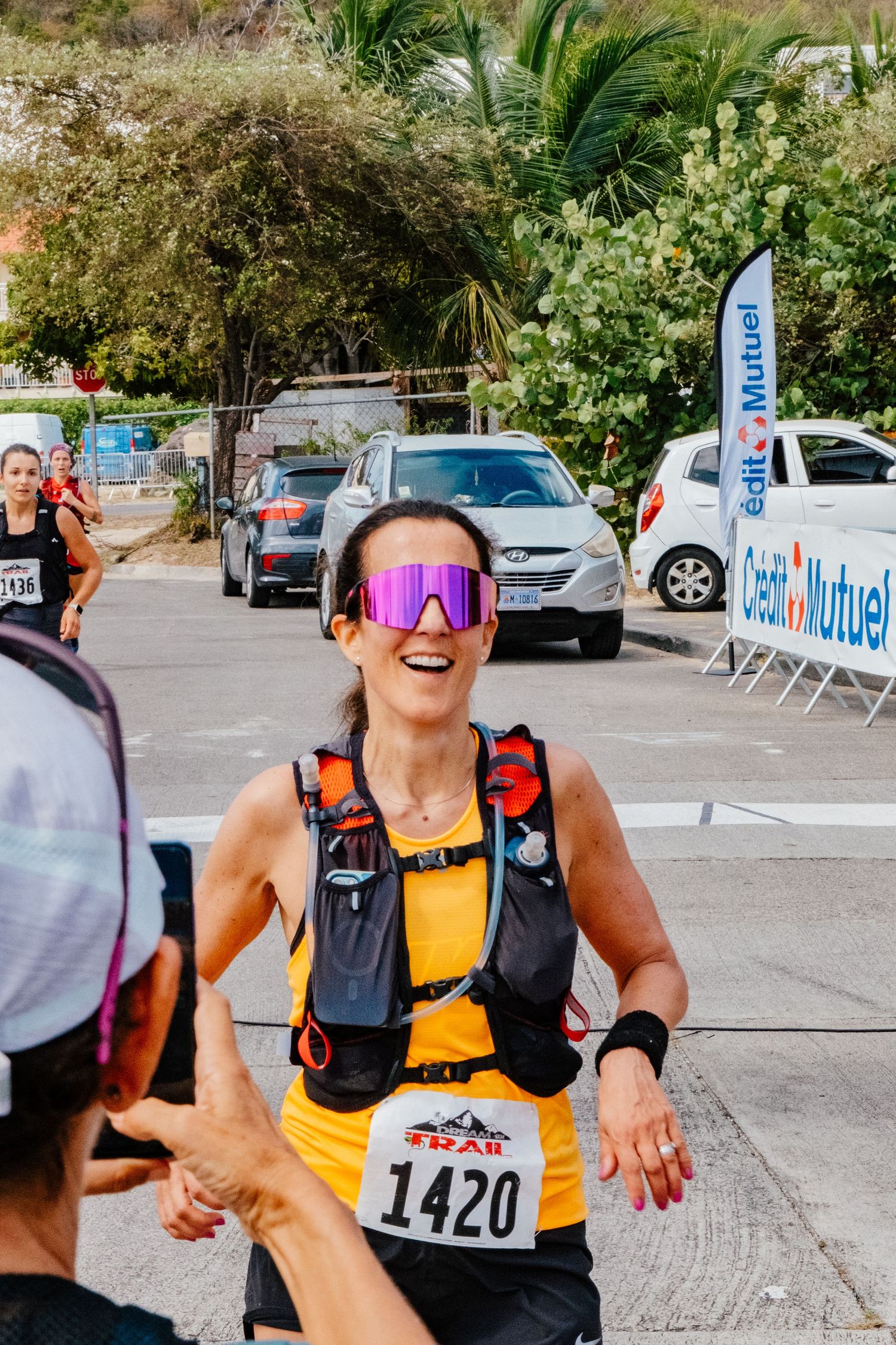 Runner wearing race number 1420 and reflective sunglasses participates in outdoor race event with tropical scenery.