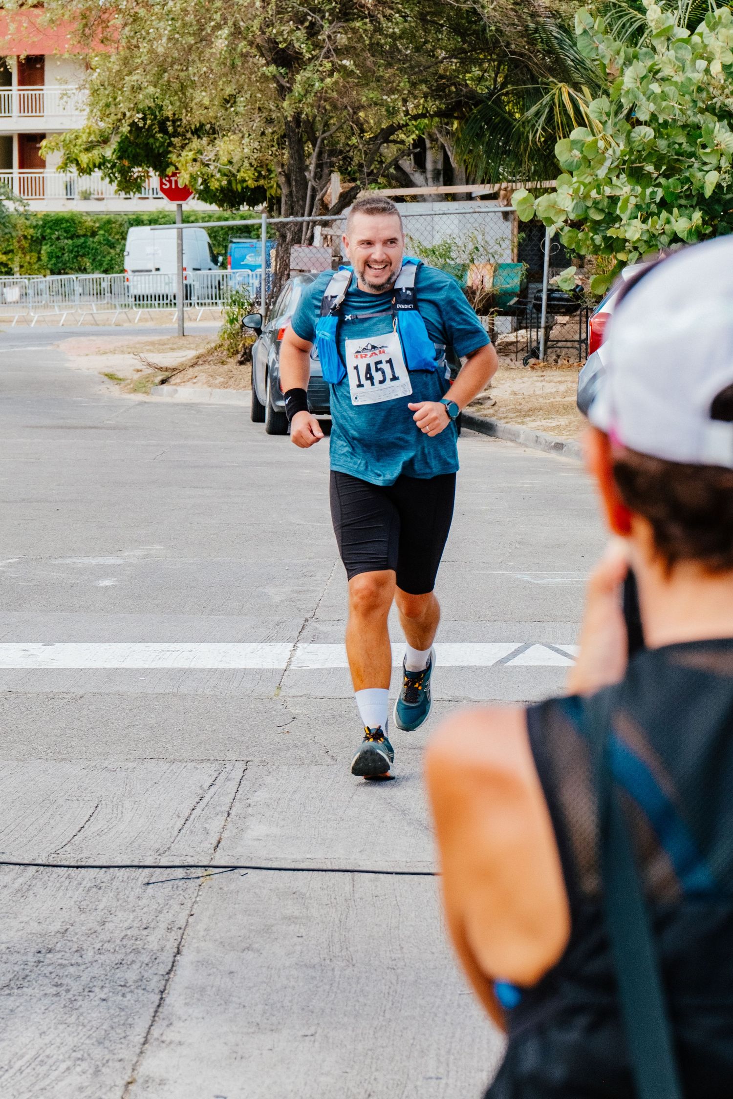 Runner wearing bib number 141 in blue shirt and black shorts competes in a road race while being photographed.