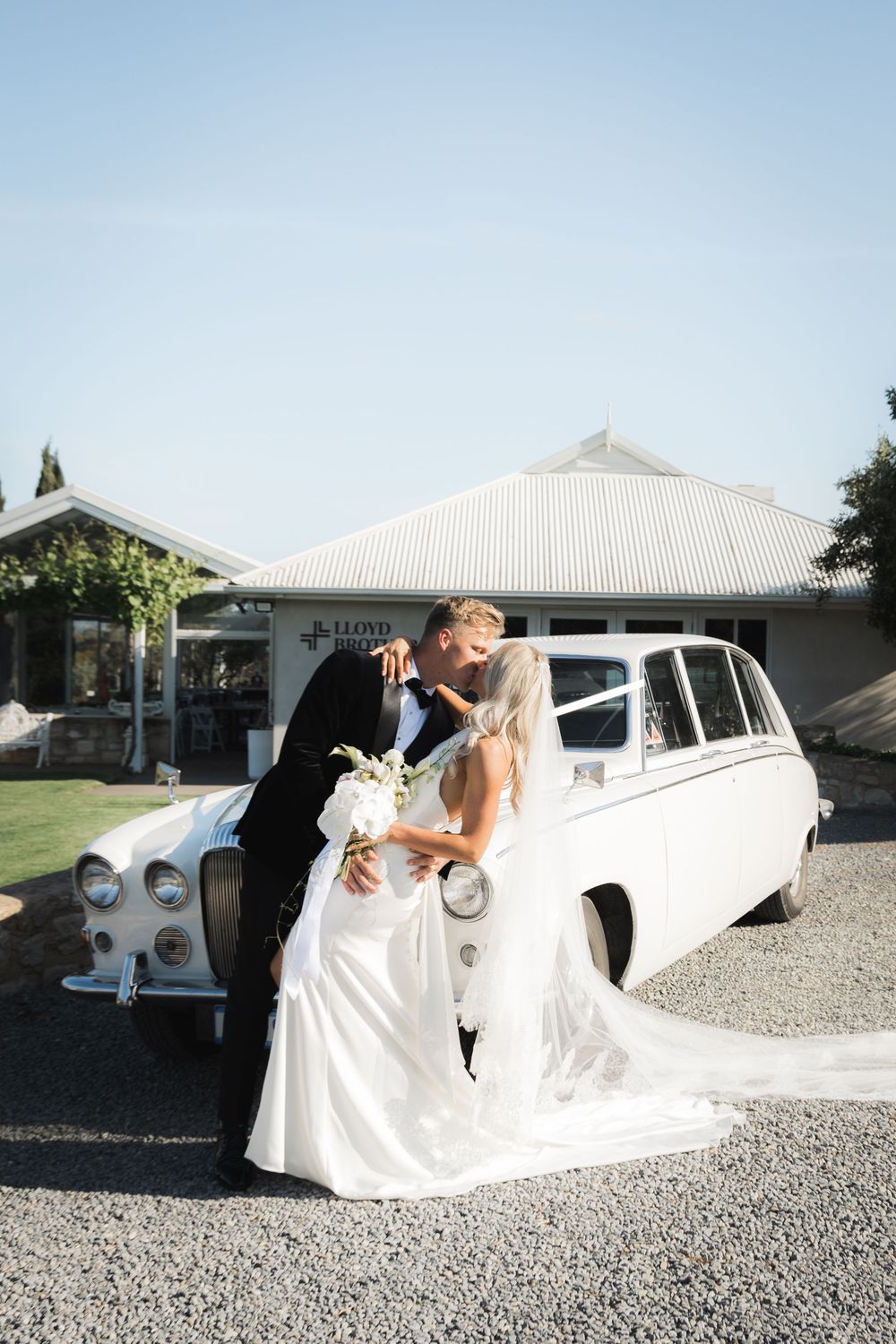 Romantic couple poses together by classic white Rolls Royce vintage car for elegant outdoor wedding photo.