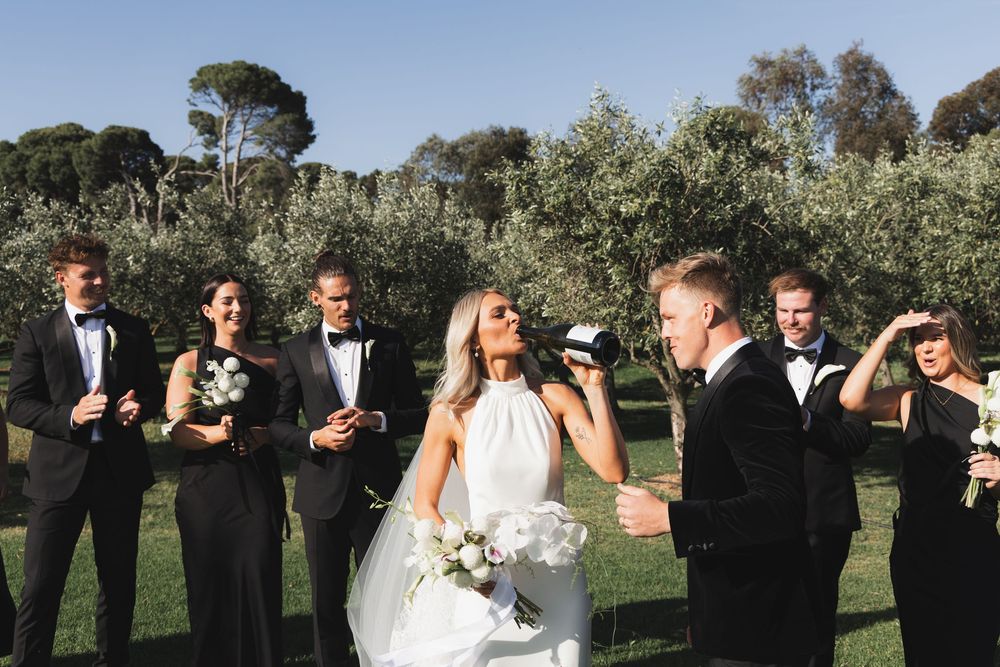 Wedding party in formal attire laughing together outdoors with bridesmaids in black and groomsmen in tuxedos.