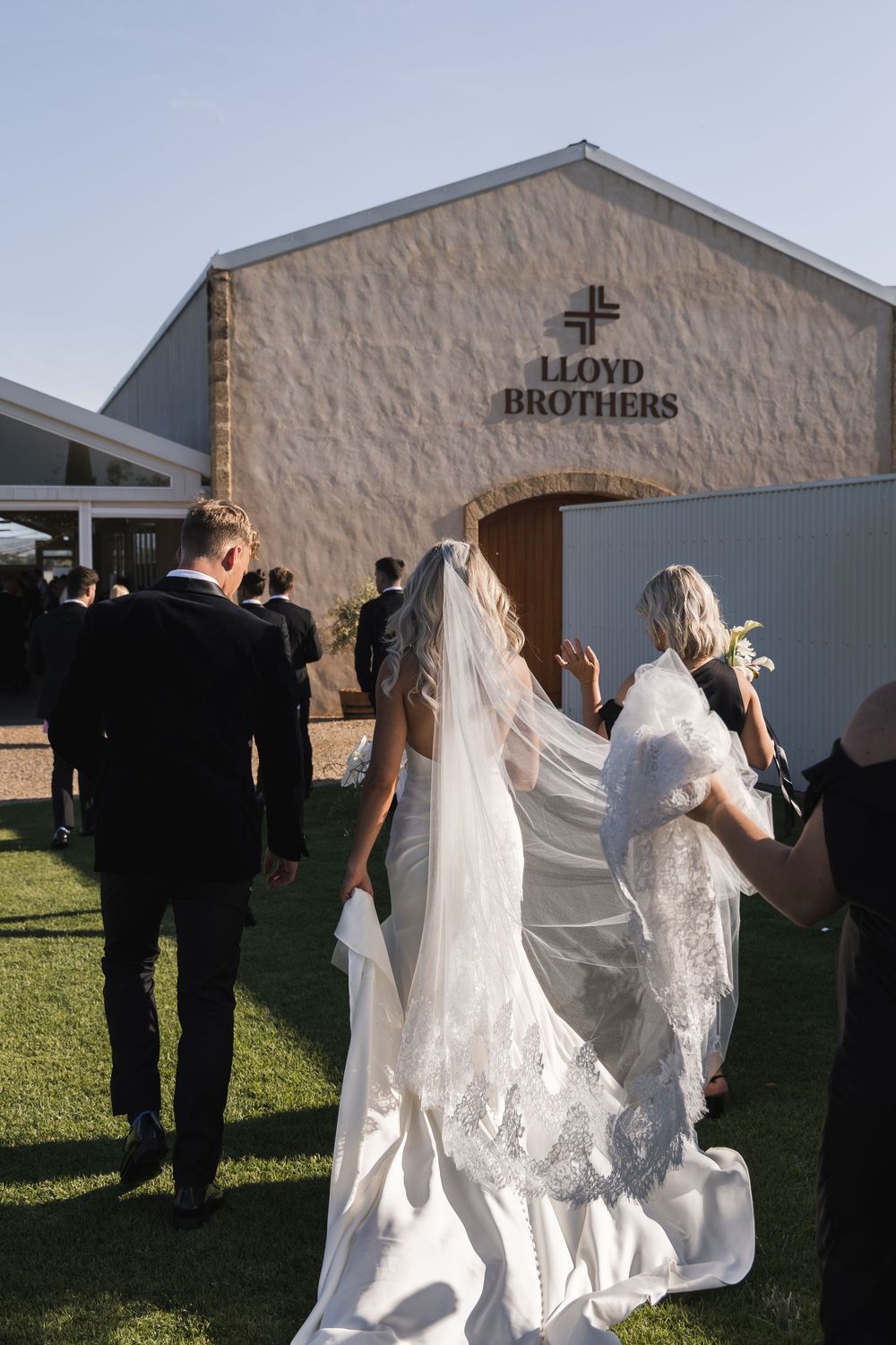 Wedding party stands outside Lloyd Brothers venue as bride's veil flows in late afternoon sunlight.