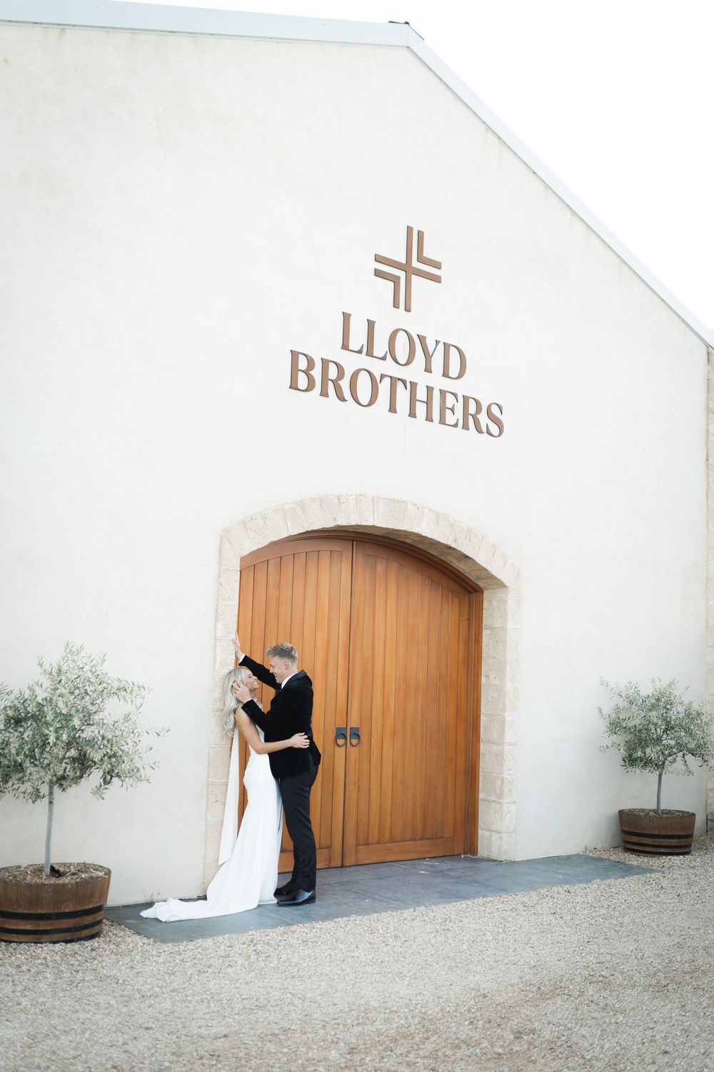 A romantic moment outside the wooden doors of Lloyd Brothers winery with decorative olive trees in planters.