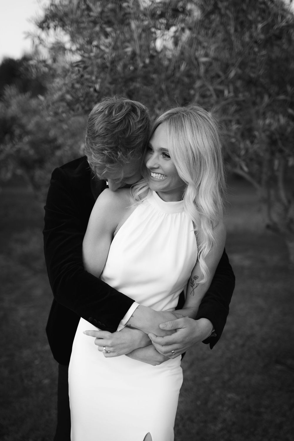 An intimate black and white portrait of an elegant couple embracing outdoors.