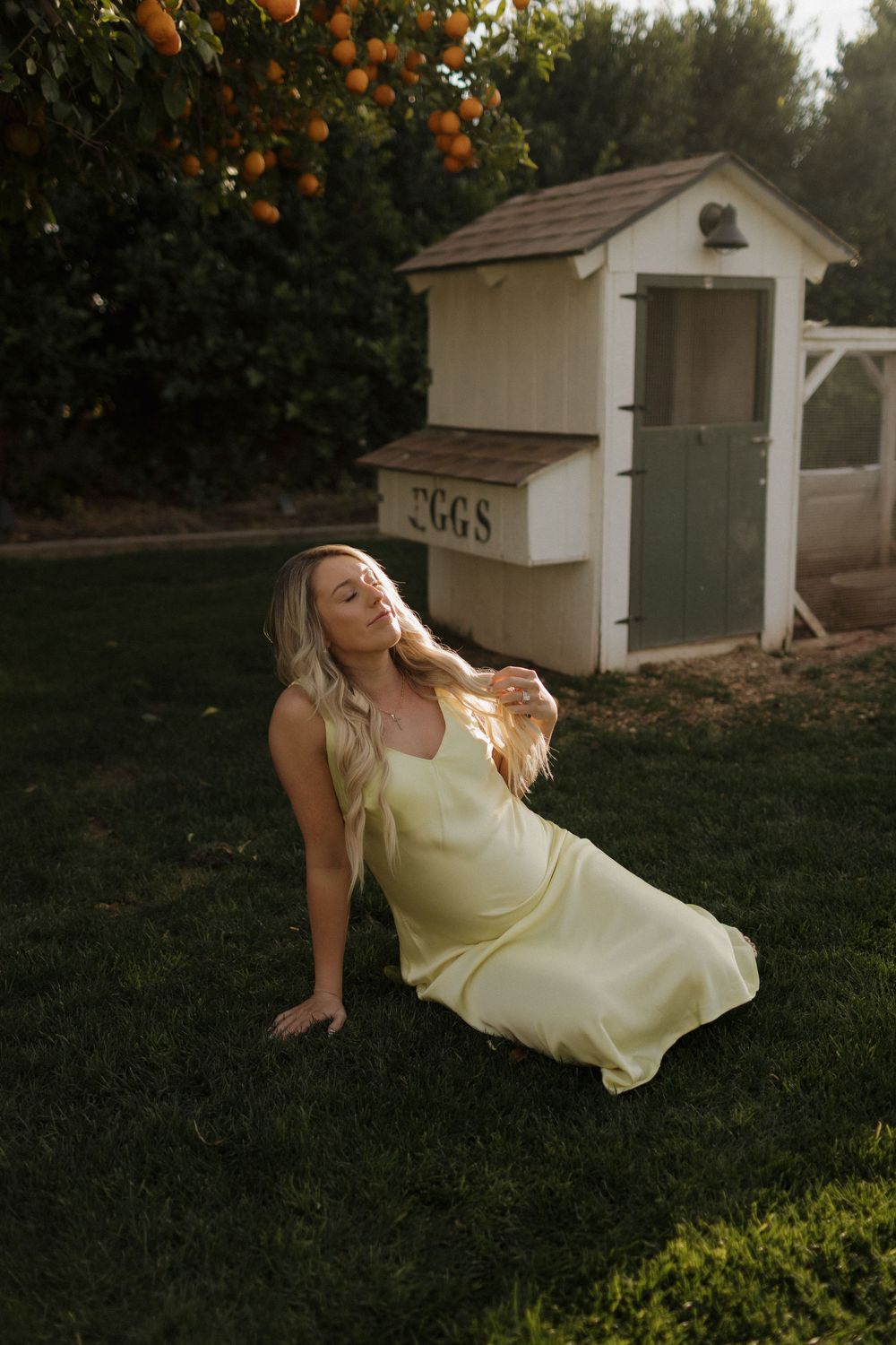 Woman in yellow dress poses gracefully against orange tree backdrop during golden hour.