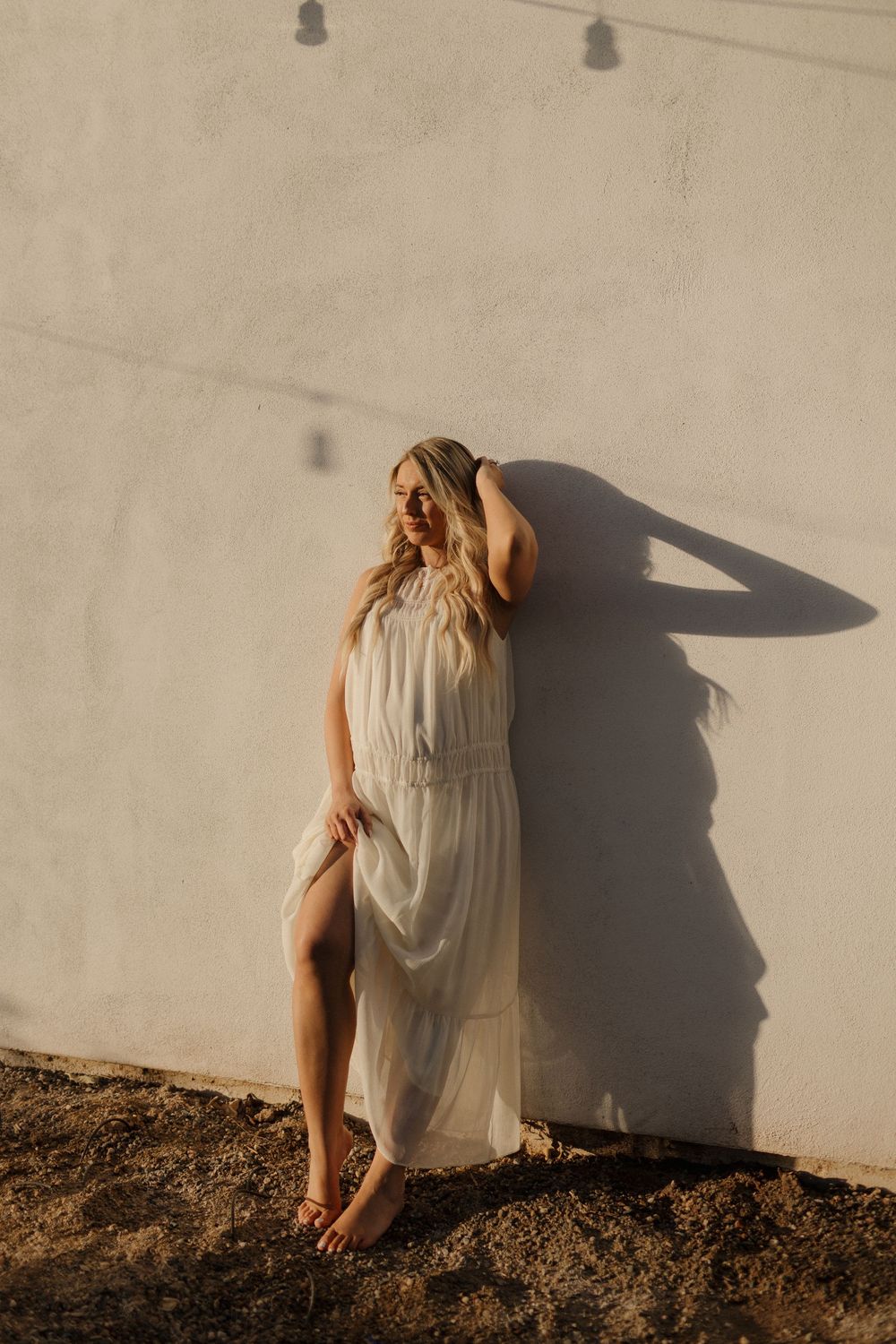 Artistic portrait against beige wall creating dramatic shadows in natural lighting.