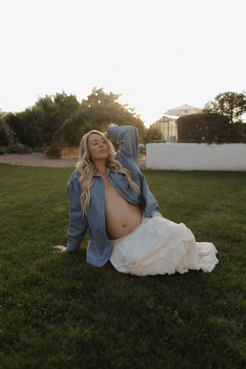A sunset photoshoot in a grassy field with denim and white dress creating a casual country aesthetic.