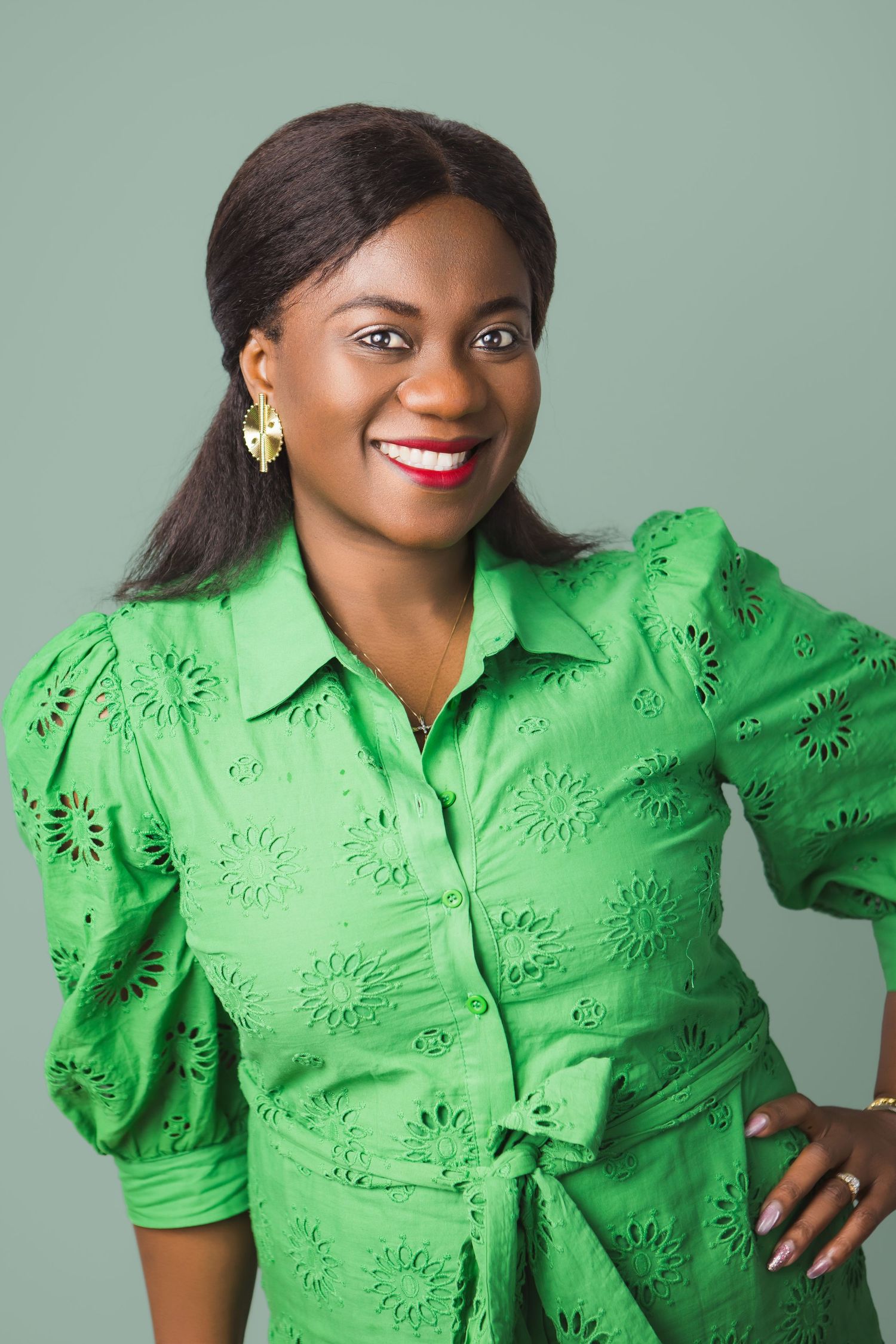 Professional studio portrait of someone wearing a bright green eyelet blouse with puff sleeves and gold earrings against gray backdrop.