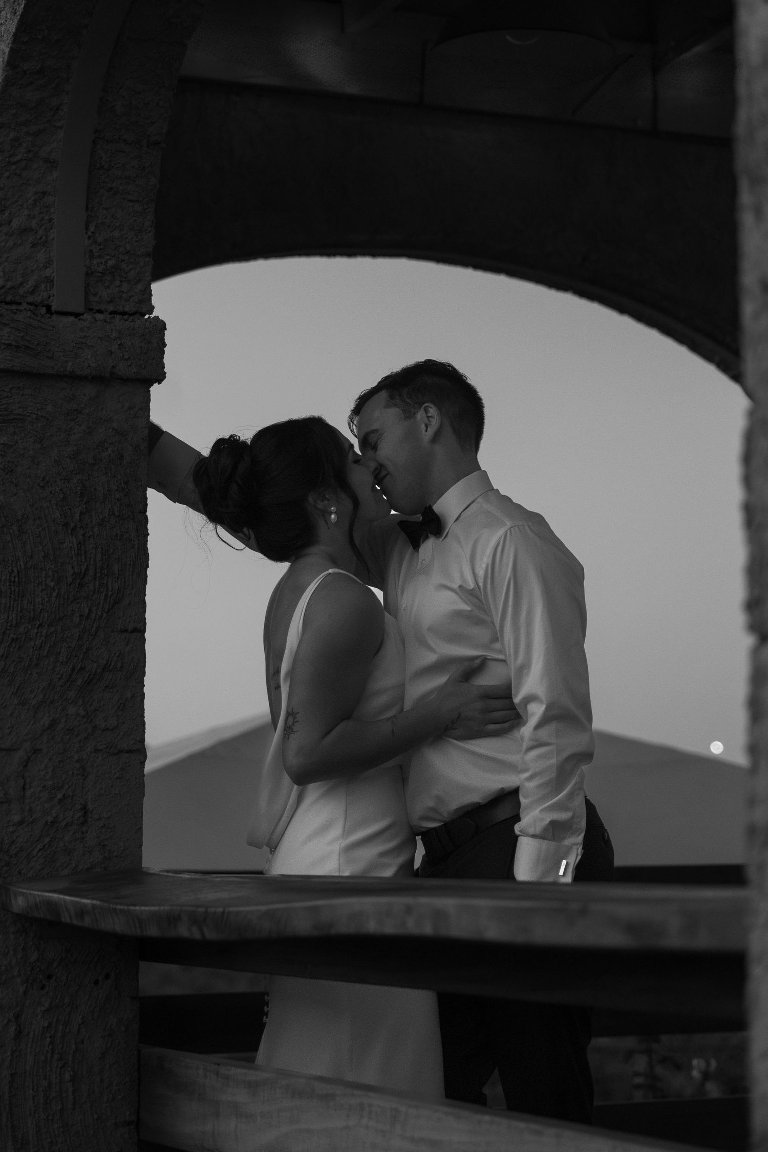 Silhouettes of a couple sharing an intimate moment at sunset through stone archways.
