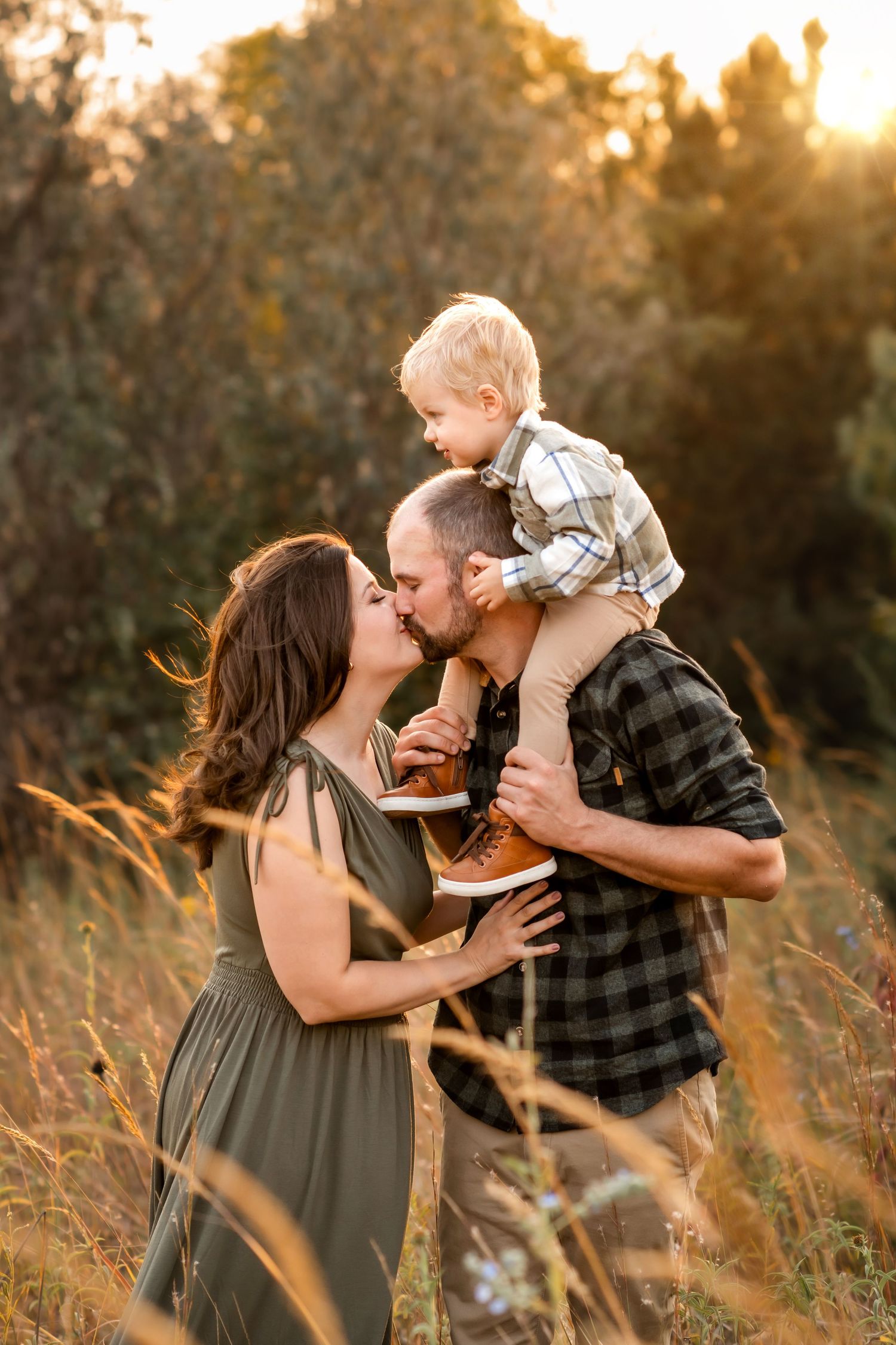 A family shares a tender moment at sunset in a golden field of tall grass.