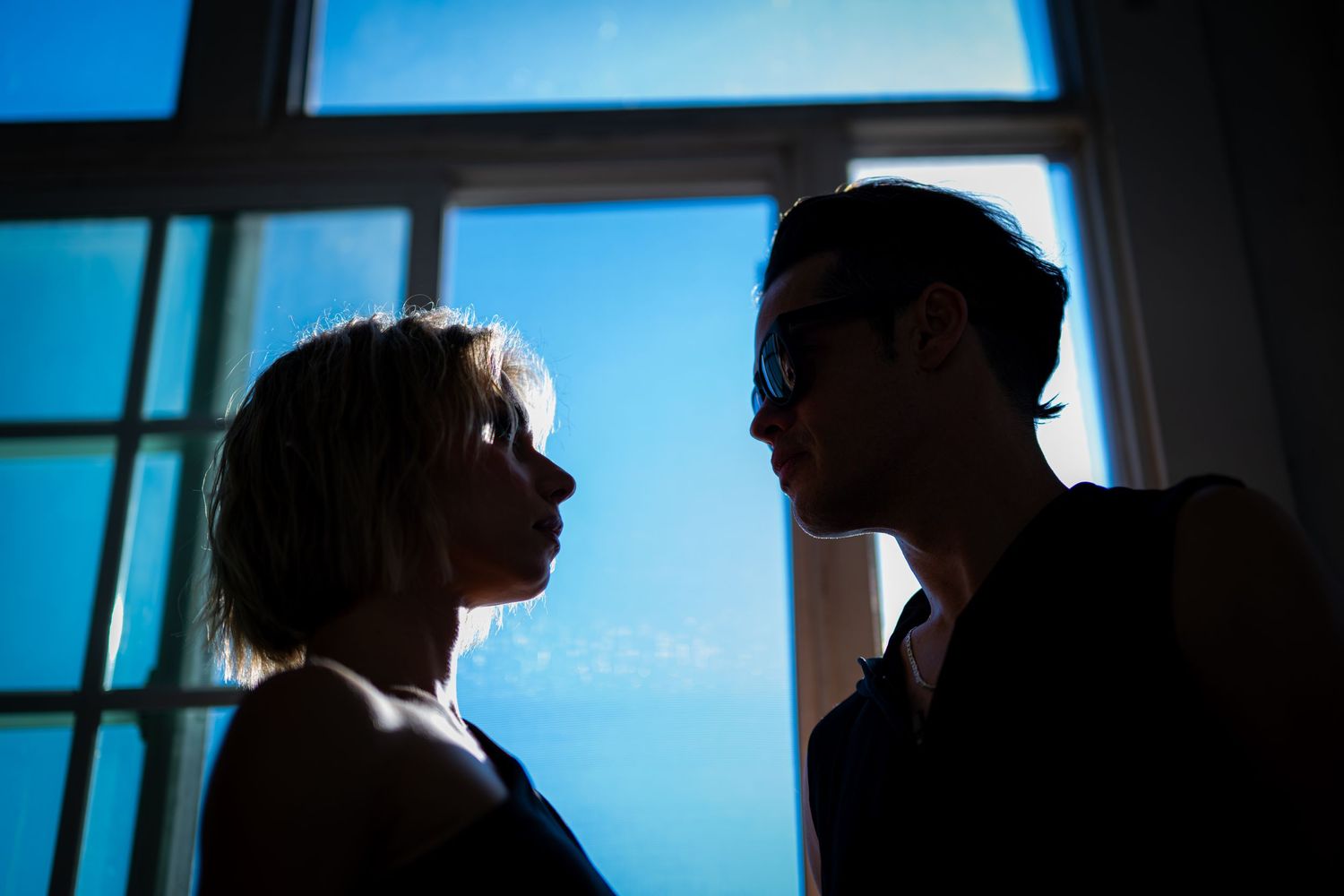 Two silhouetted figures share an intimate moment against a blue-tinted window backdrop.