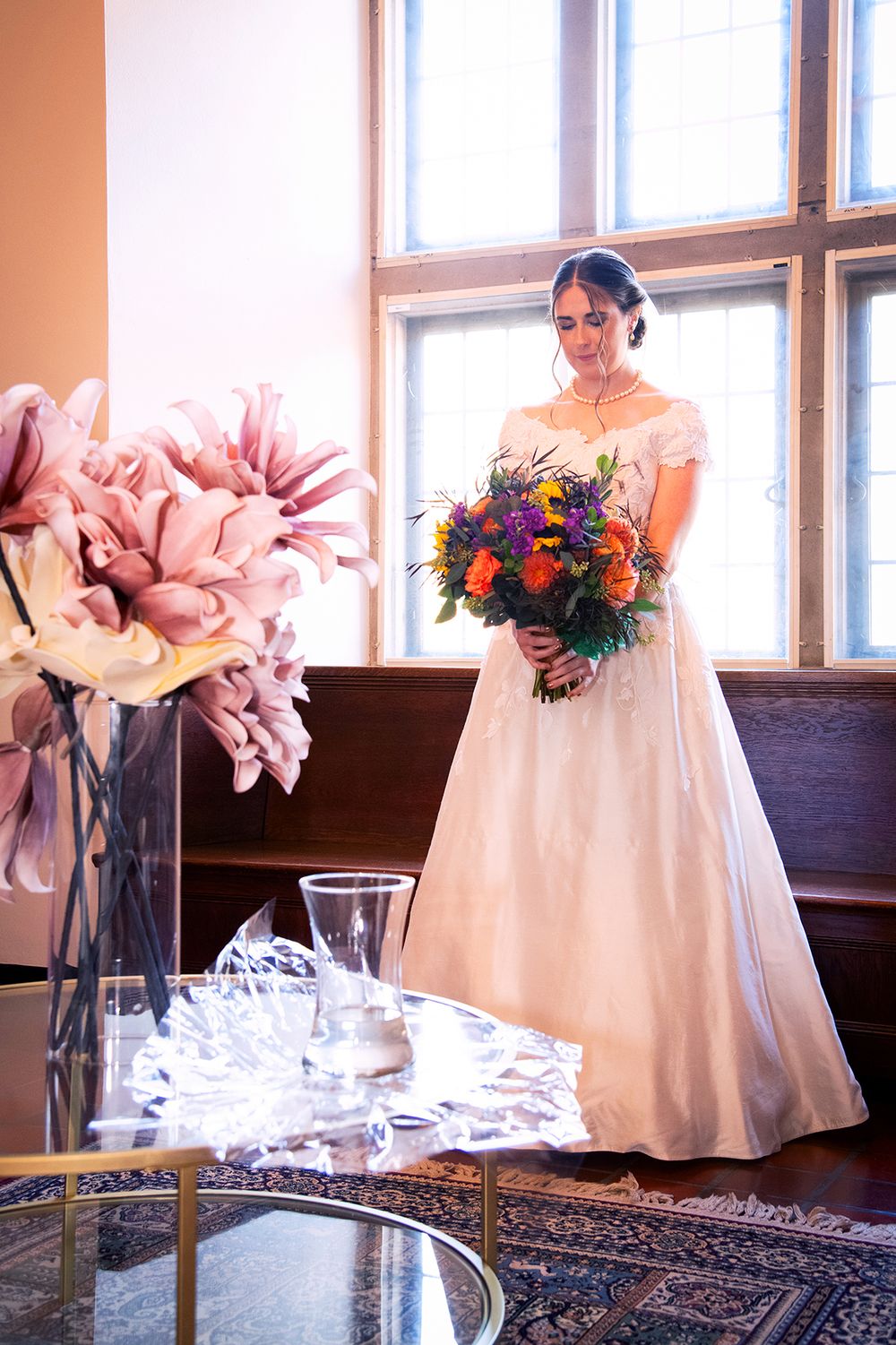 A traditional wedding with a white gown and vibrant purple bouquet by large windows and elegant floral decor. (Highland Park Rochester NY)