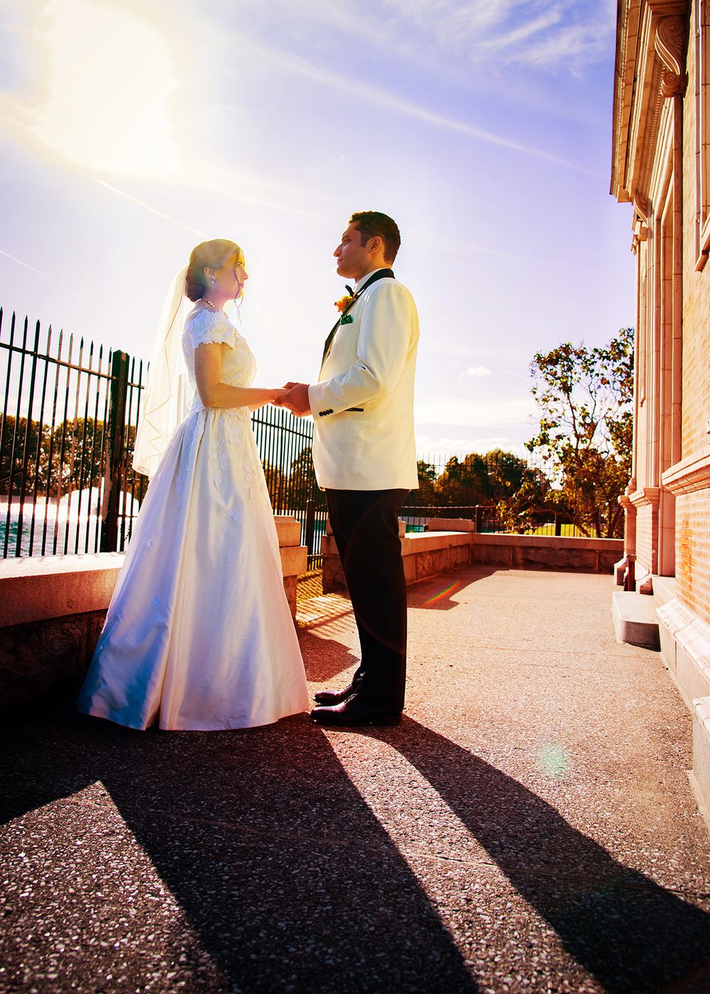 A couple shares a romantic moment at sunset on a grand porch with elegant white columns and iron railings. (Highland Park Rochester NY)