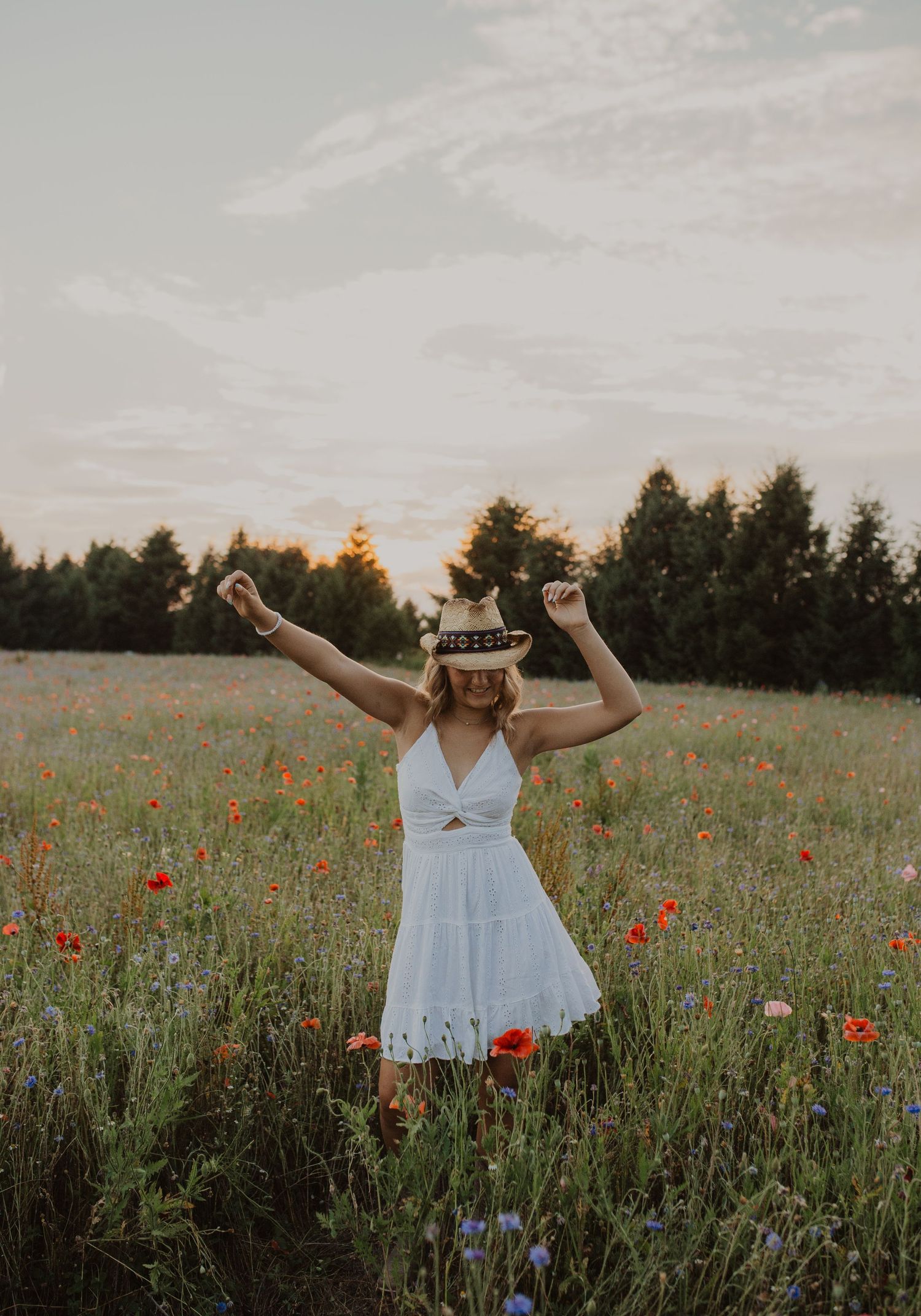 Joyful pose in white dress among colorful wildflowers at golden hour.