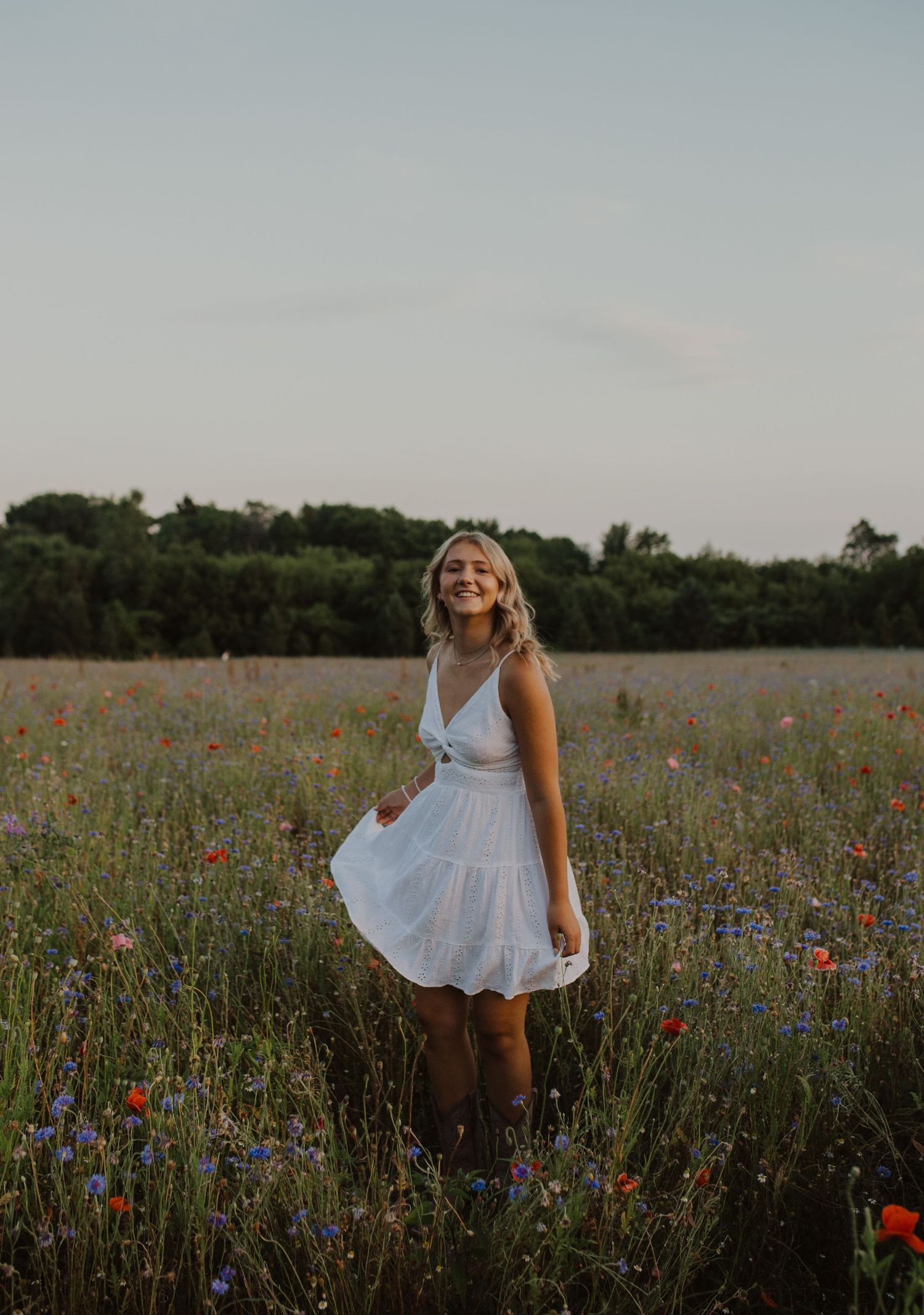 A white sundress flows in the breeze as someone twirls in a wildflower meadow filled with red poppies and blue flowers.