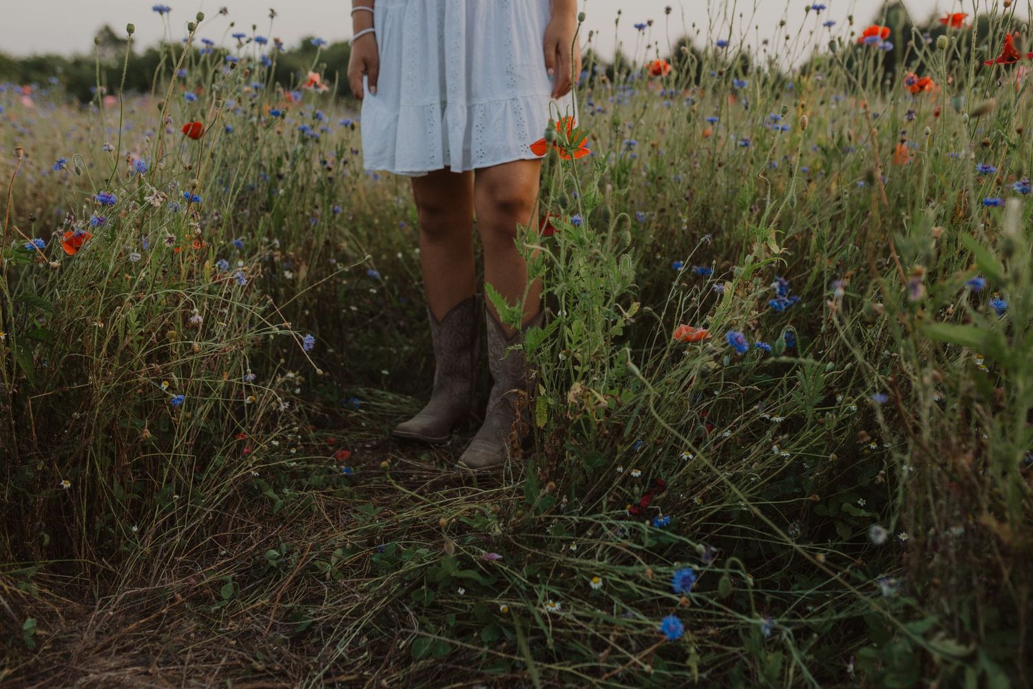 Brown boots stand among wild grasses and flowers in a natural meadow setting.