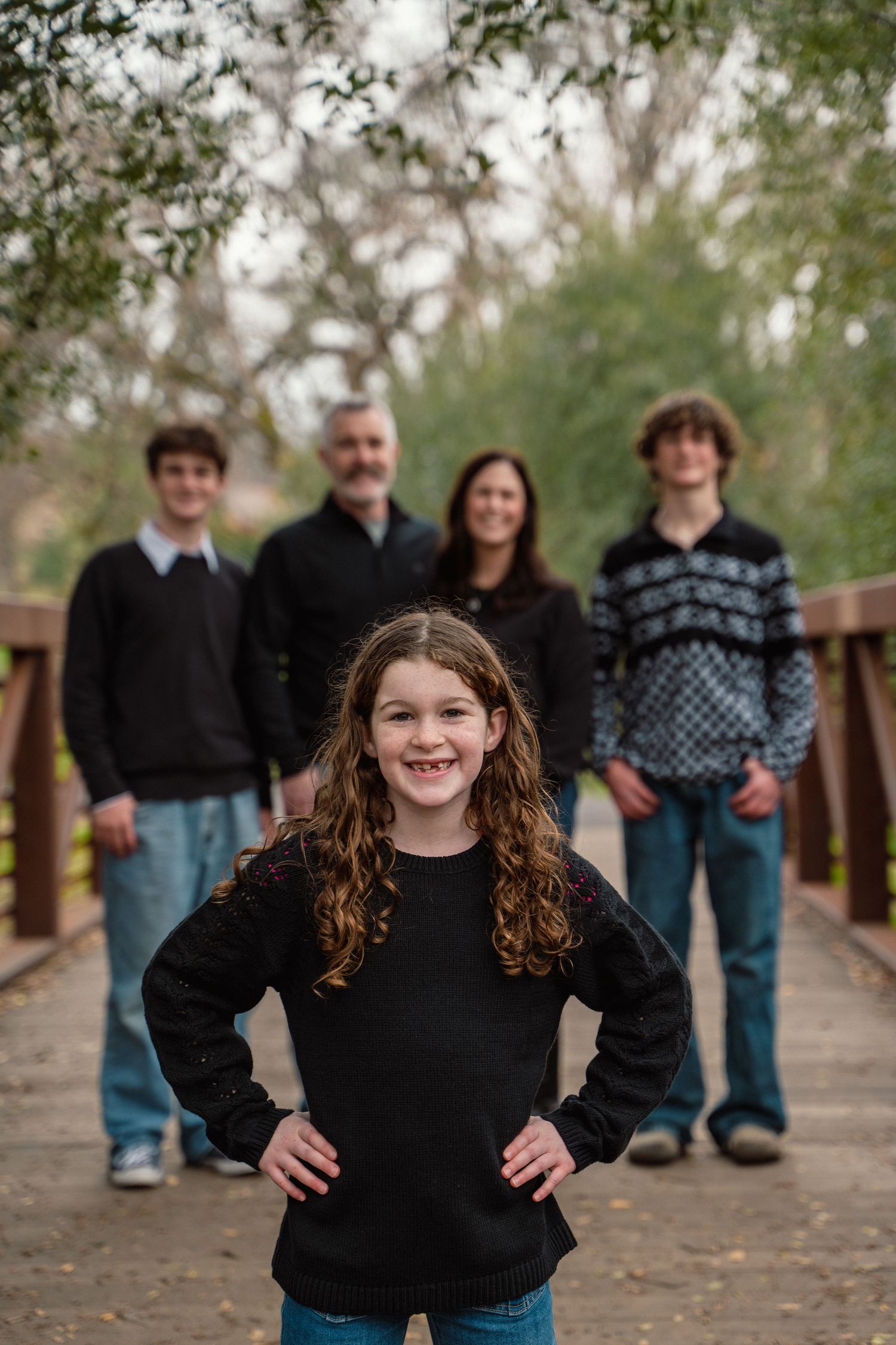 A family portrait of five people standing on a wooden bridge surrounded by trees.