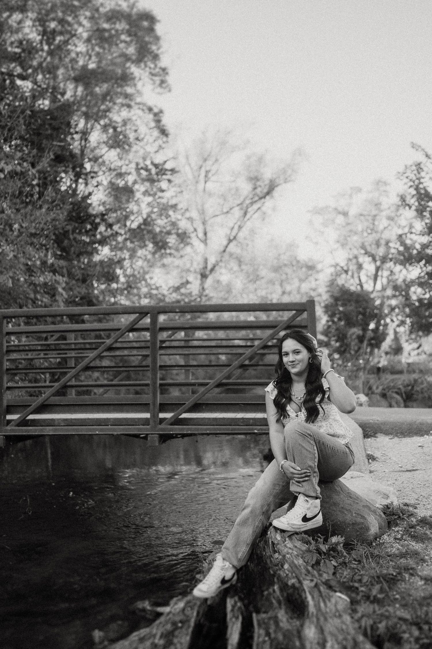 Black and white portrait taken on a rock by a rustic bridge with natural scenery in the background.