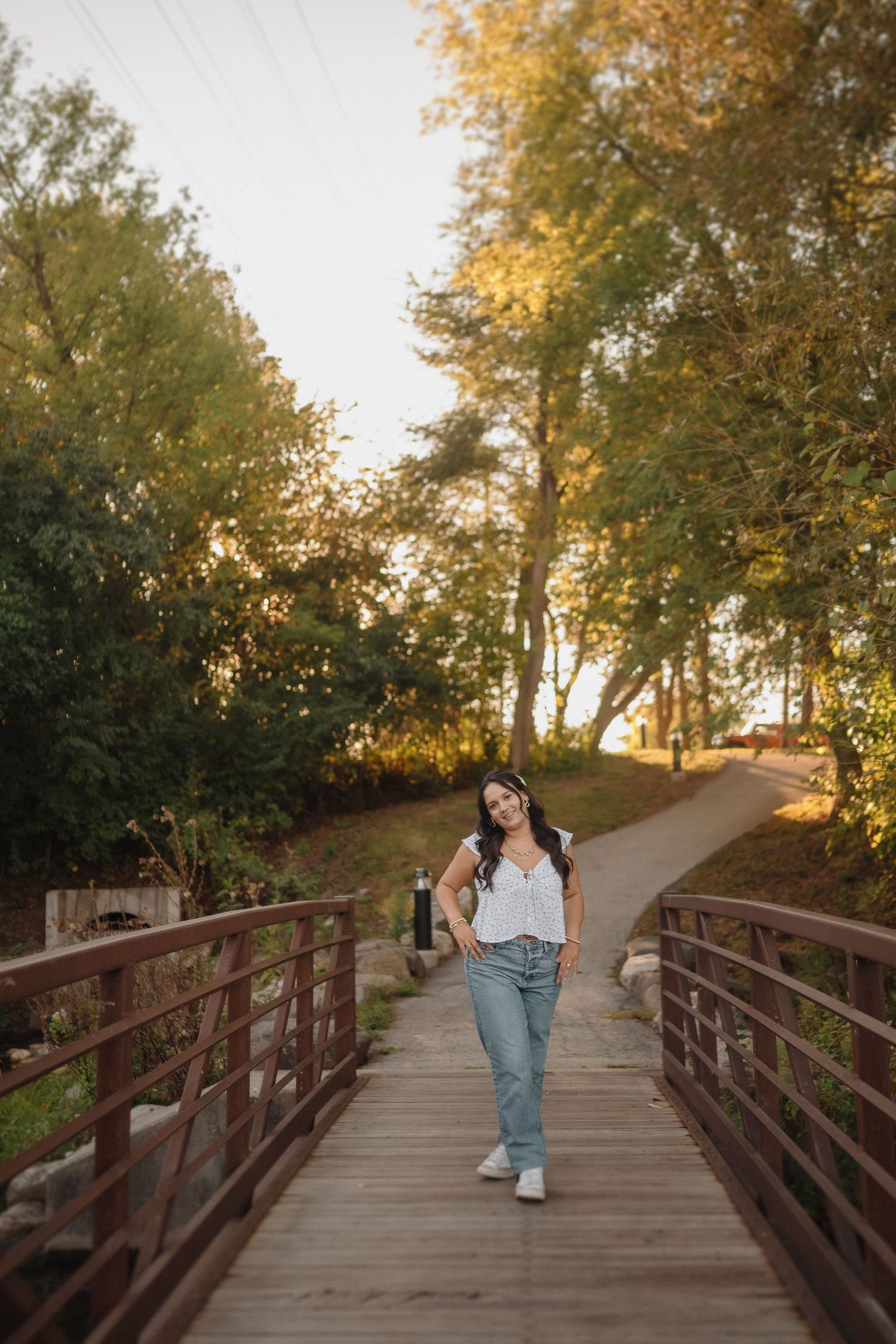 A person in casual wear walks across a wooden bridge surrounded by autumn trees during golden hour sunset.