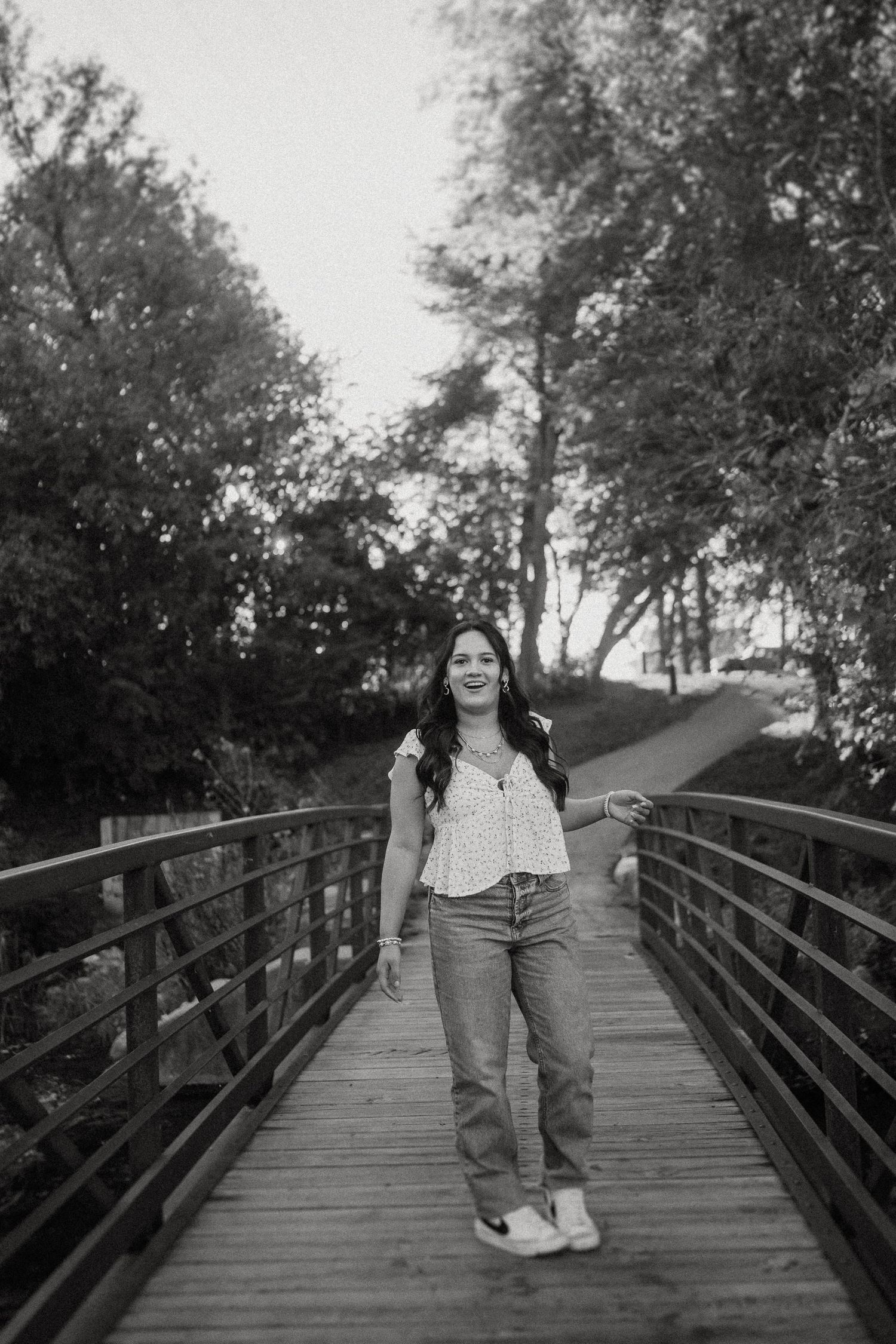 A joyful figure strolls along a rustic wooden bridge surrounded by trees in a black and white photograph.